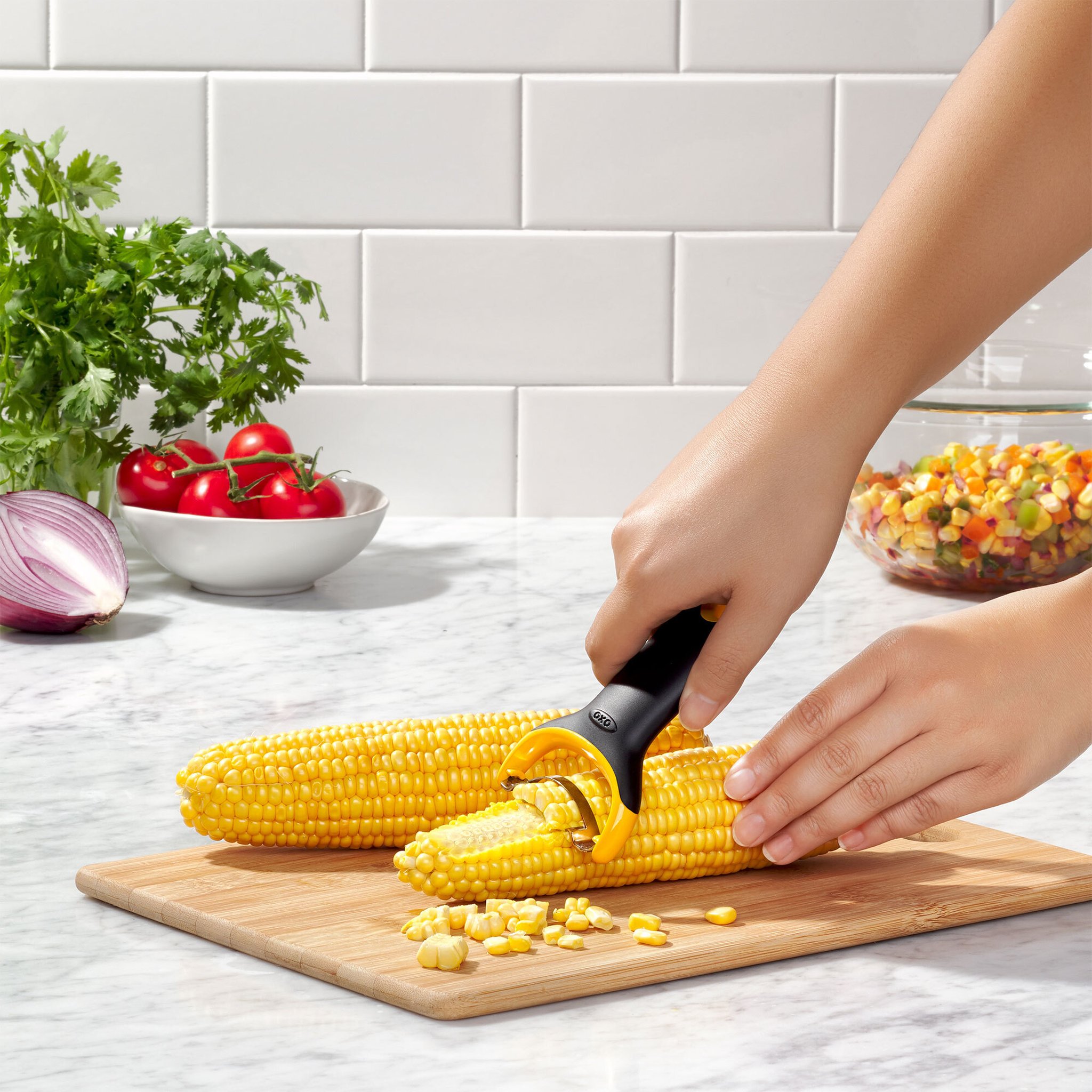 Hände lösen mit dem OXO Maiskolbenschäler die Körner von einem Maiskolben auf dem Schneidebrett