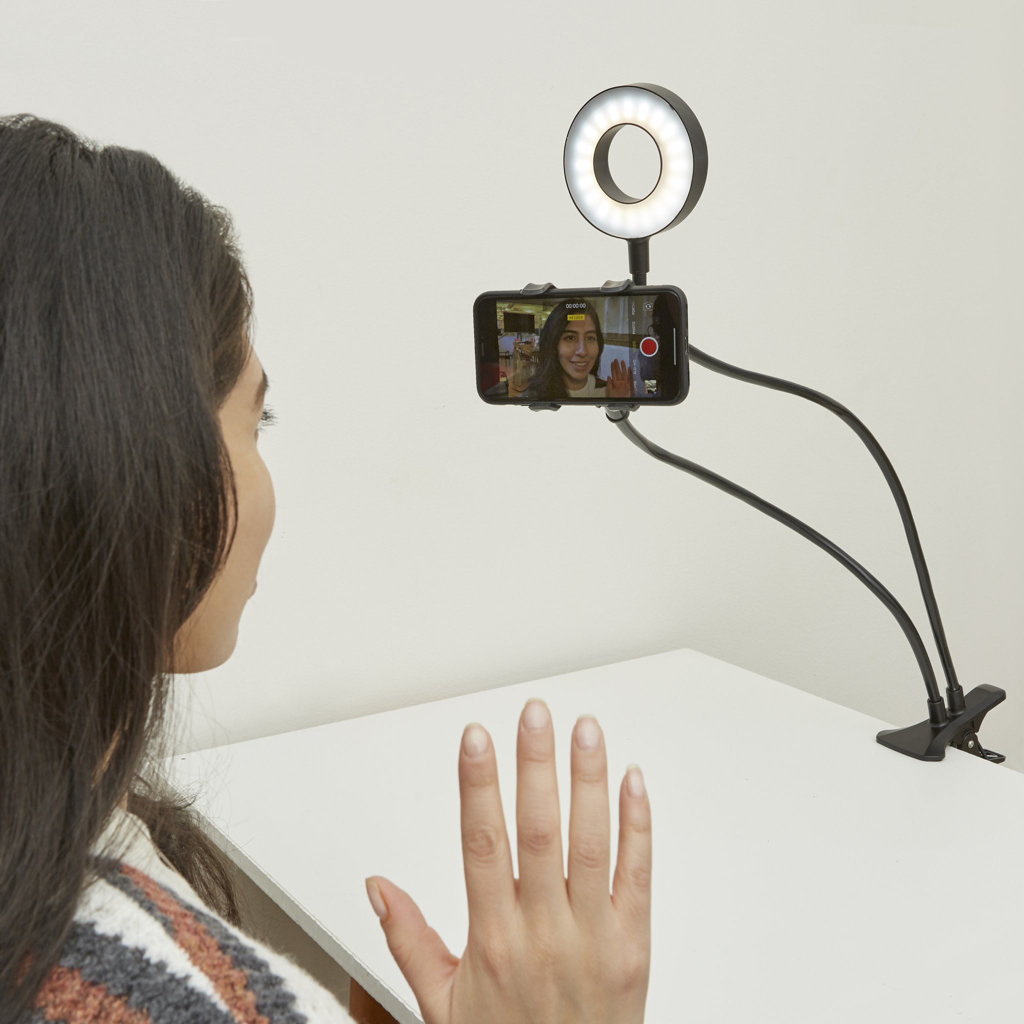 Live streaming kit clamped to the table, woman waving at the smartphone