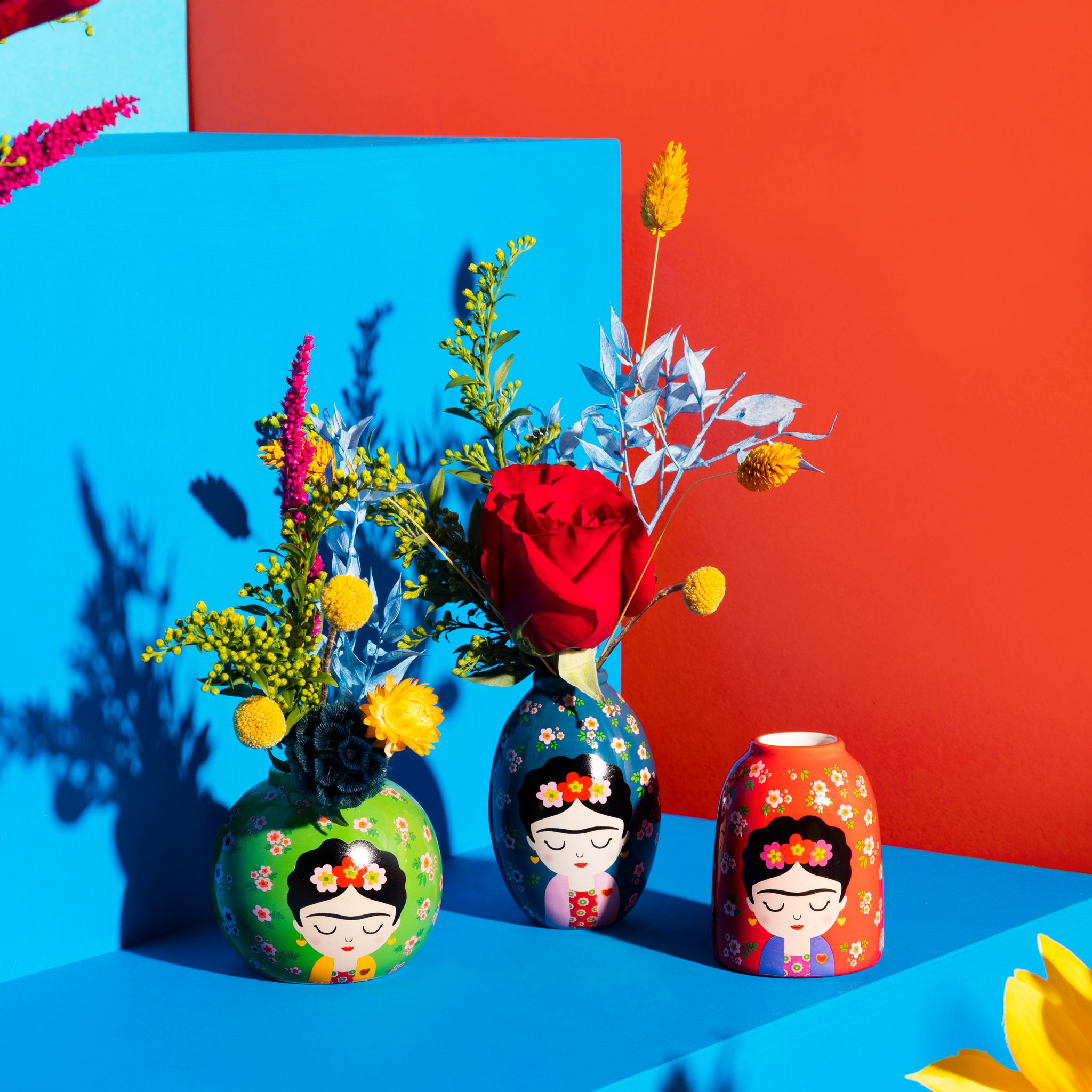 Frida Vasen-Set von Sass & Belle, drei Vasen mit Blumen vor blau-orangem Hintergrund