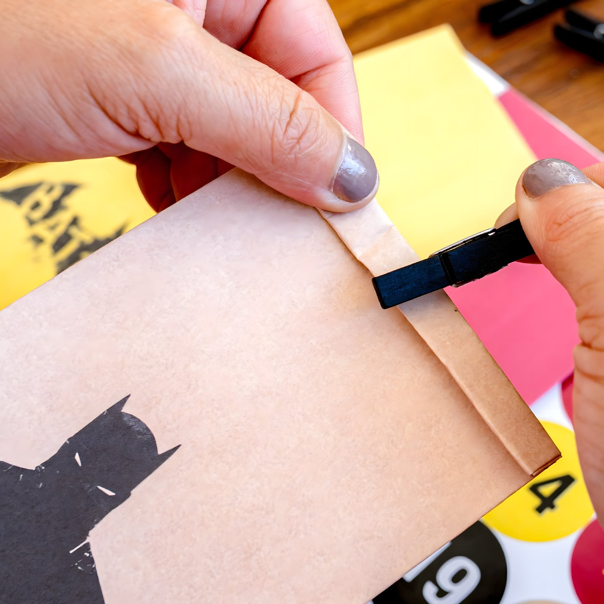 Hände verschliessen eine Kraftpapiertüte mit Batman-Motiv mit einer schwarzen Holzklammer