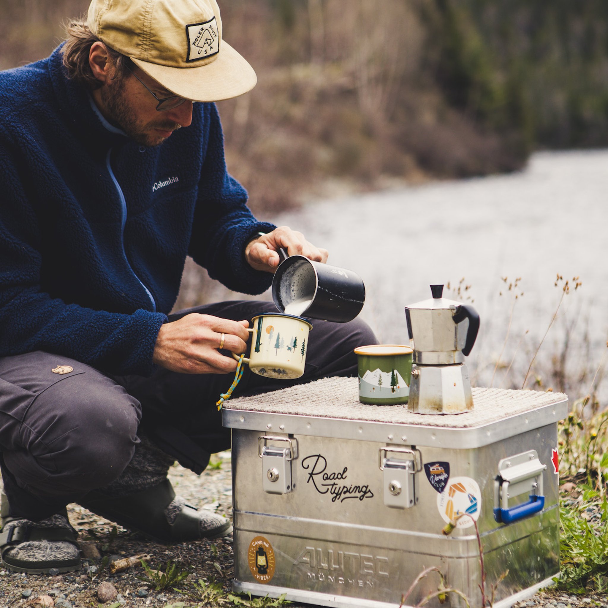 Emaillebecher beim Kochen am Campingtisch neben einer Espressokanne