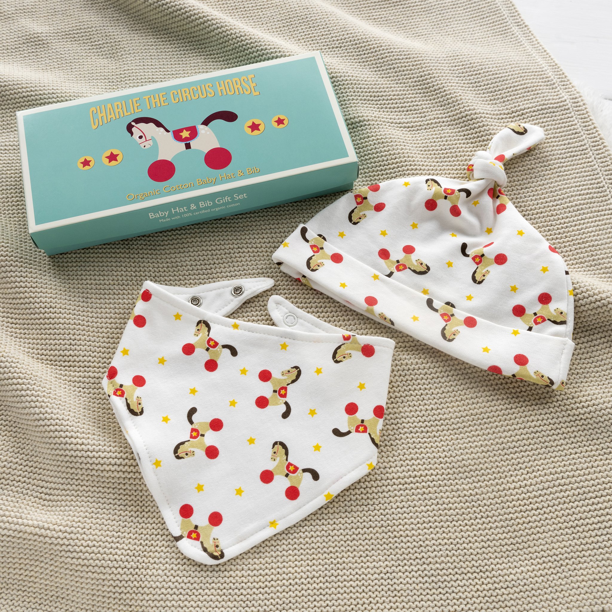 Set bavoir et bonnet bébé Charlie sur une couverture tricotée à côté du coffret
