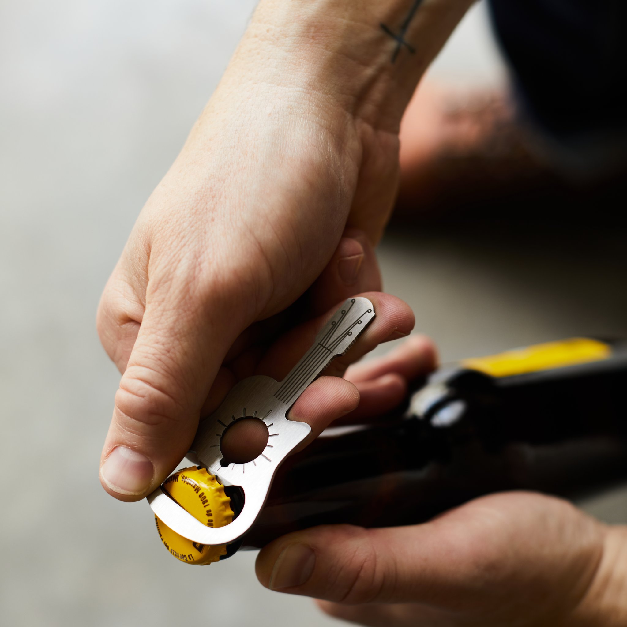 Close-up of the mini guitar bottle opener levering a yellow cap off the beer bottle