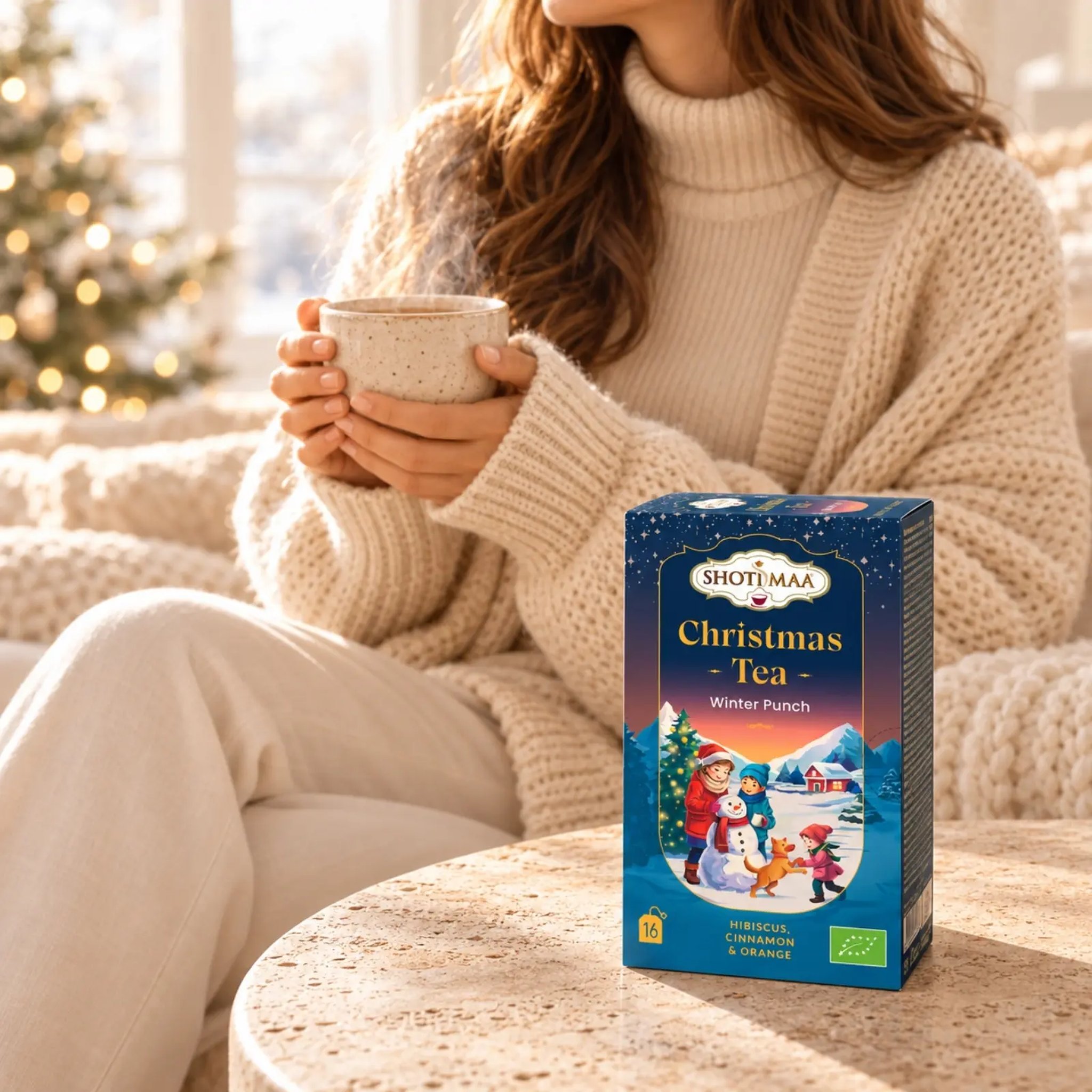Woman in a knitted jumper holding a tea cup, with the Winter Punch box in front
