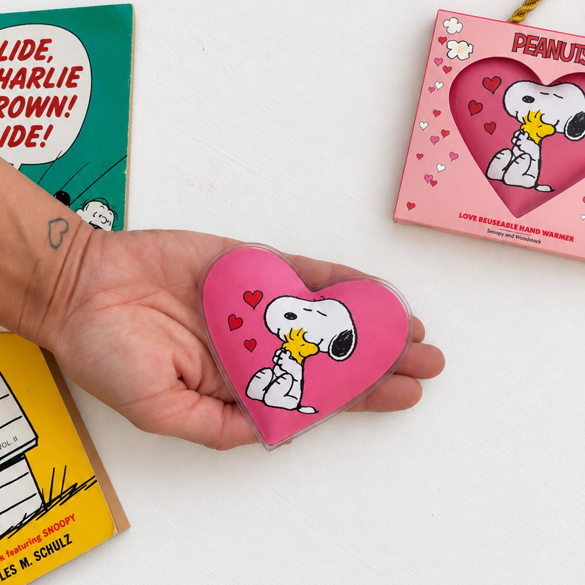 Herz-Handwärmer mit Snoopy und Woodstock in der Hand neben der Verpackung