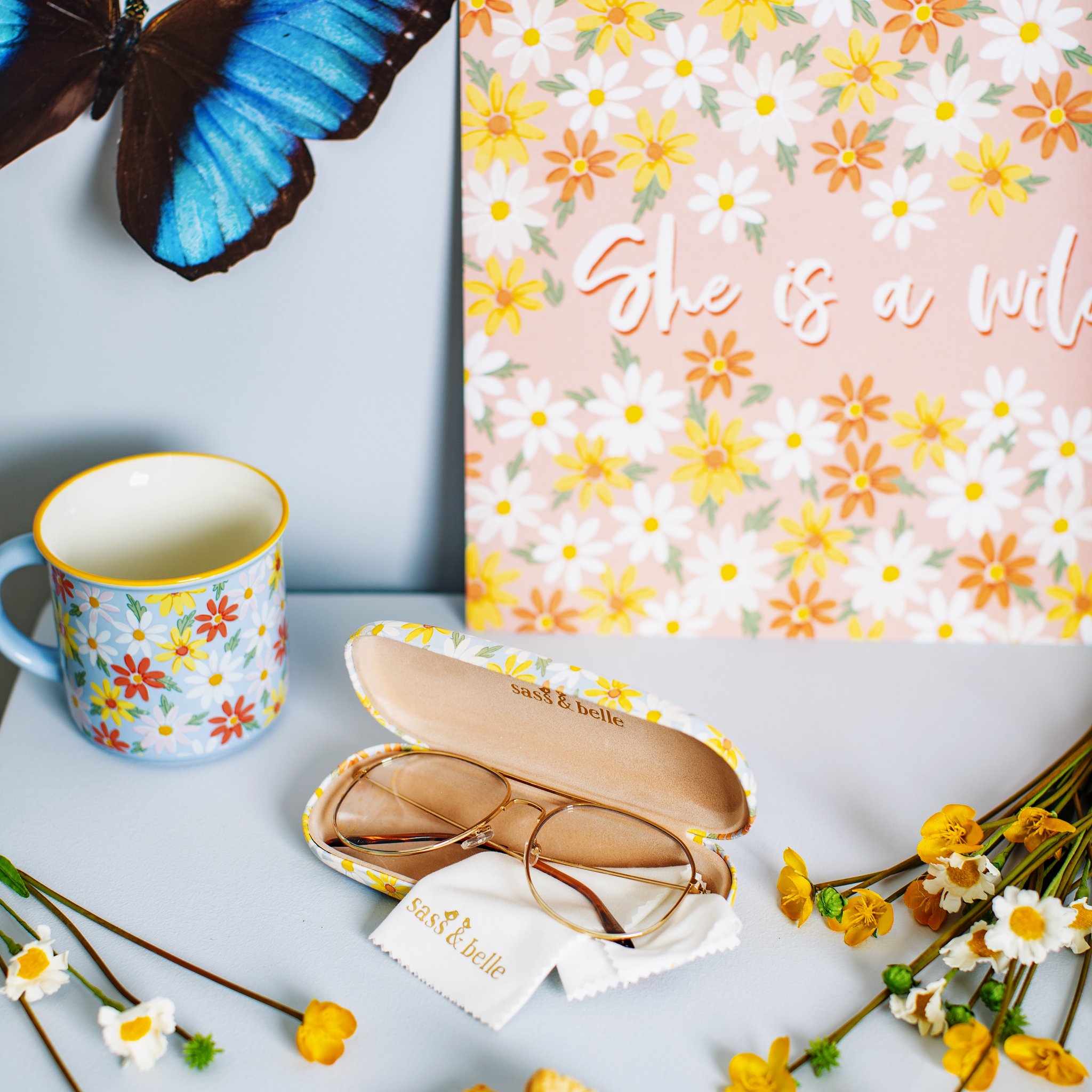 Daisy glasses case opened with glasses, next to a mug and a daisy card
