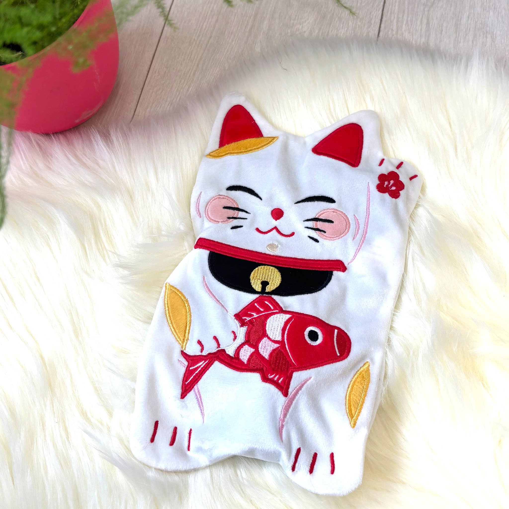 Hot water bottle shaped like a beckoning cat on a white faux fur throw