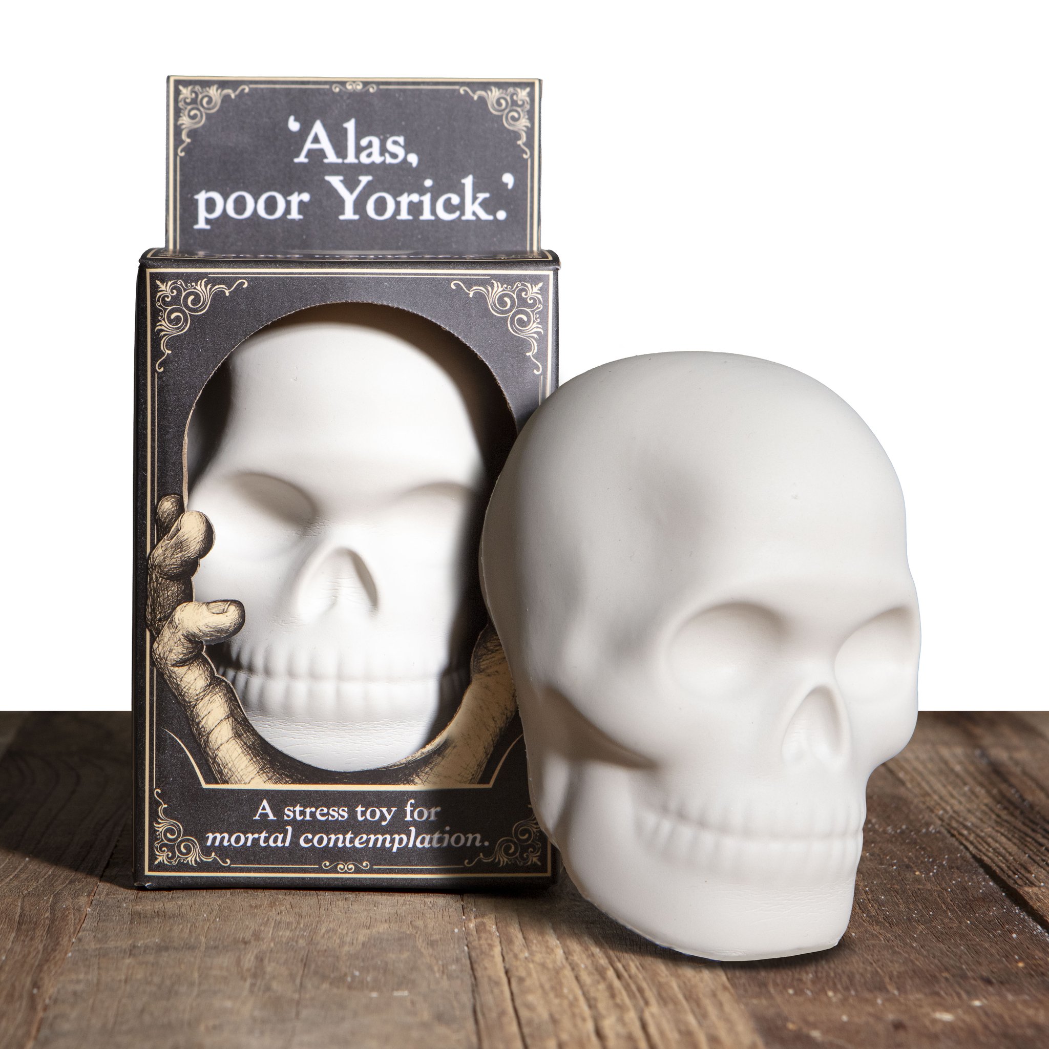 Alas Poor Yorick Totenkopf-Squishy in Cremeweiss neben der Geschenkbox mit Sichtfenster auf Holztisch