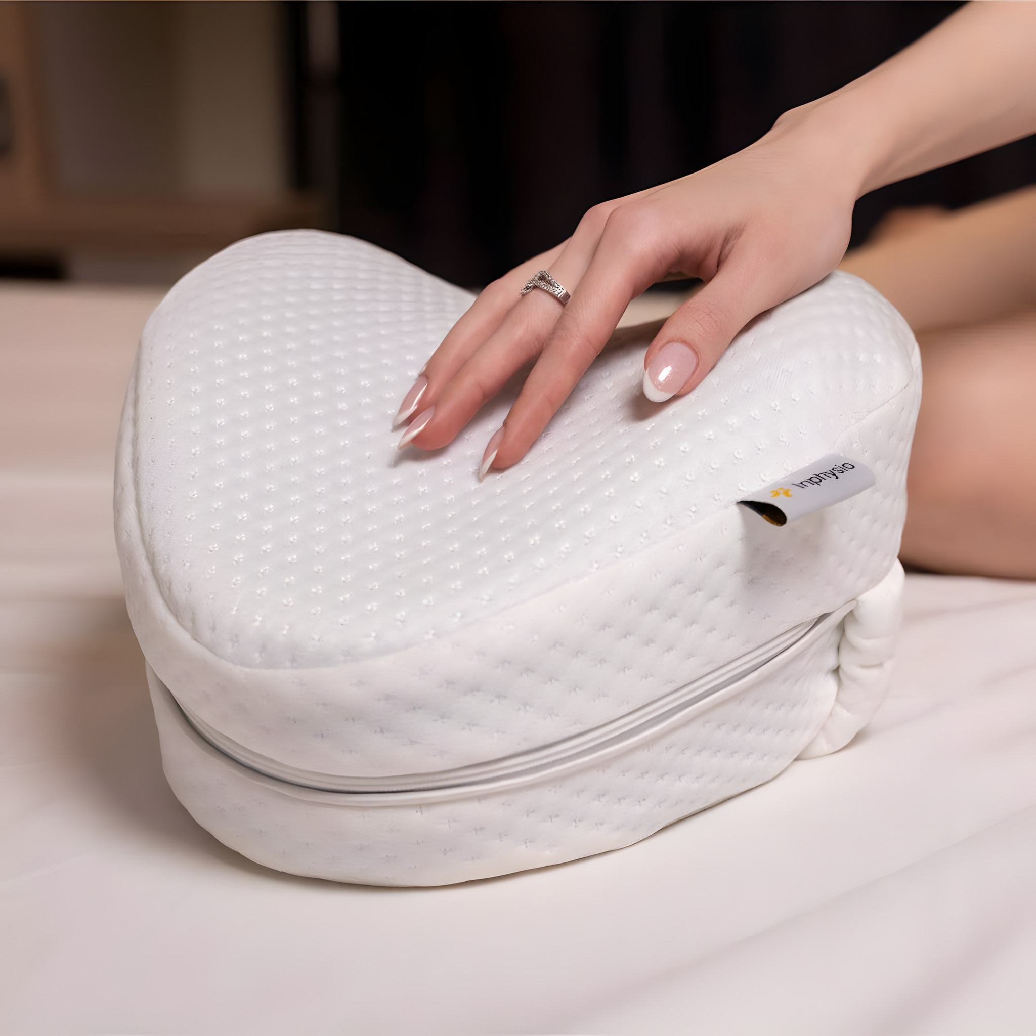 Hand auf dem herzförmigen Knie-Kissen mit elastischem Halteband auf einem Bett