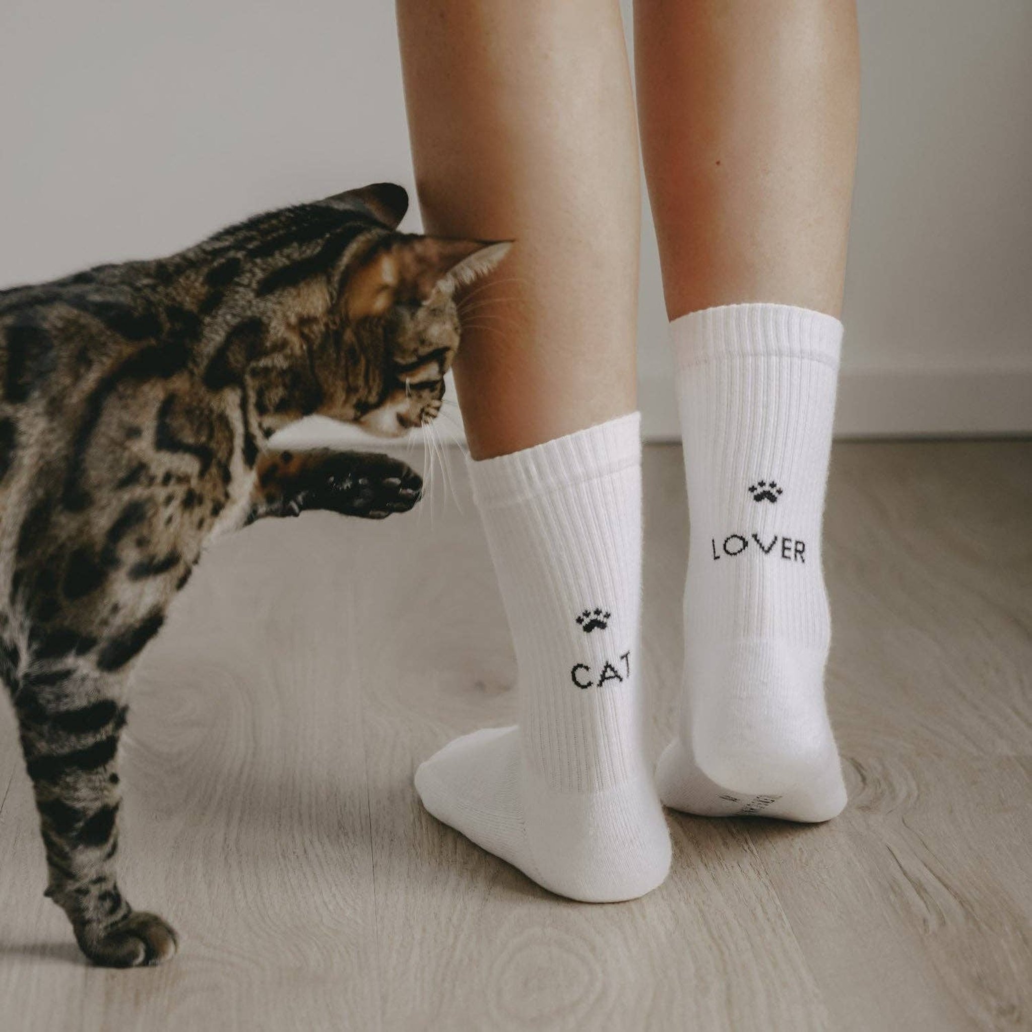 Weisse Socken Cat Lover mit Pfote und Schriftzug CAT und LOVER, daneben eine gefleckte Katze