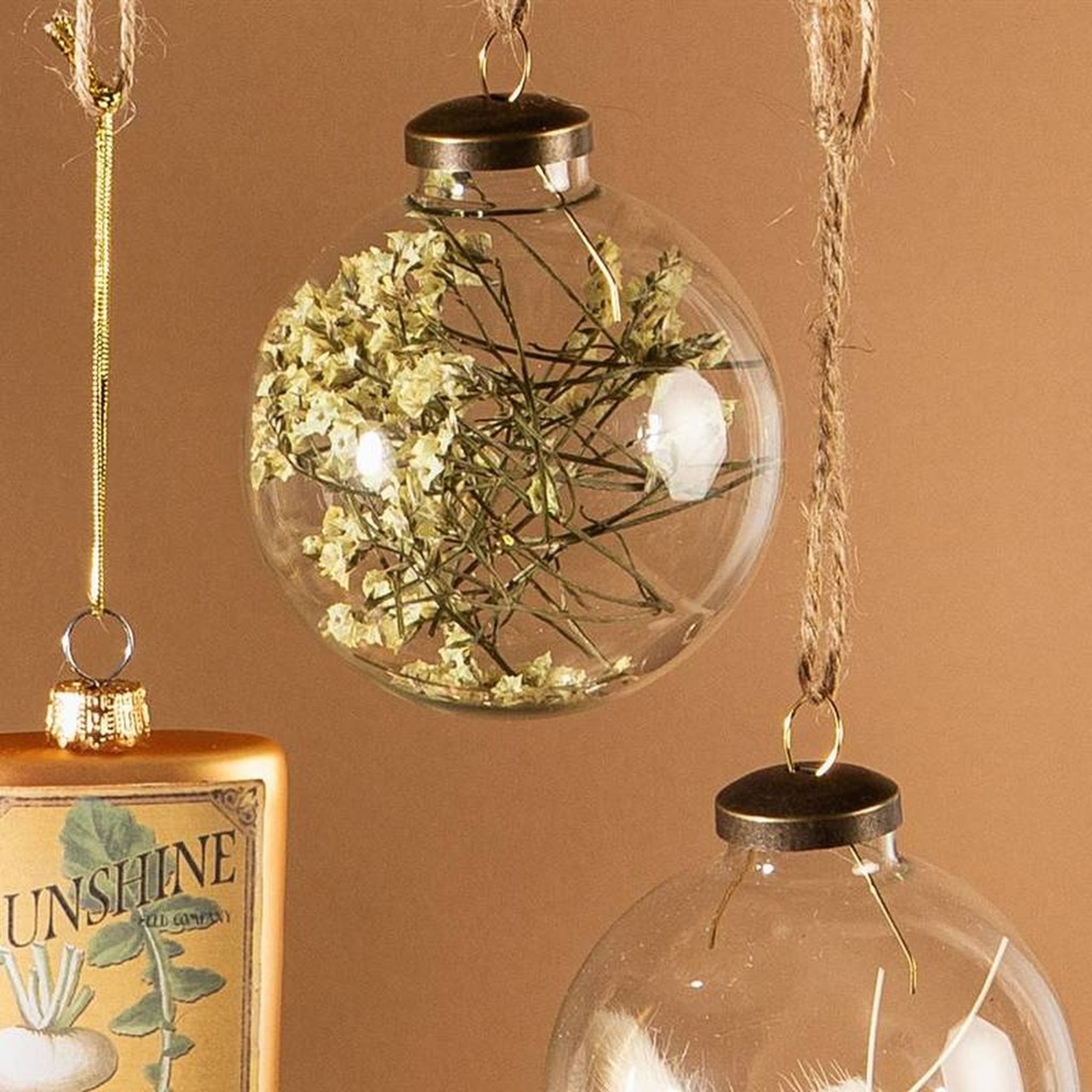Dried flower Christmas bauble hanging next to other glass baubles, close-up