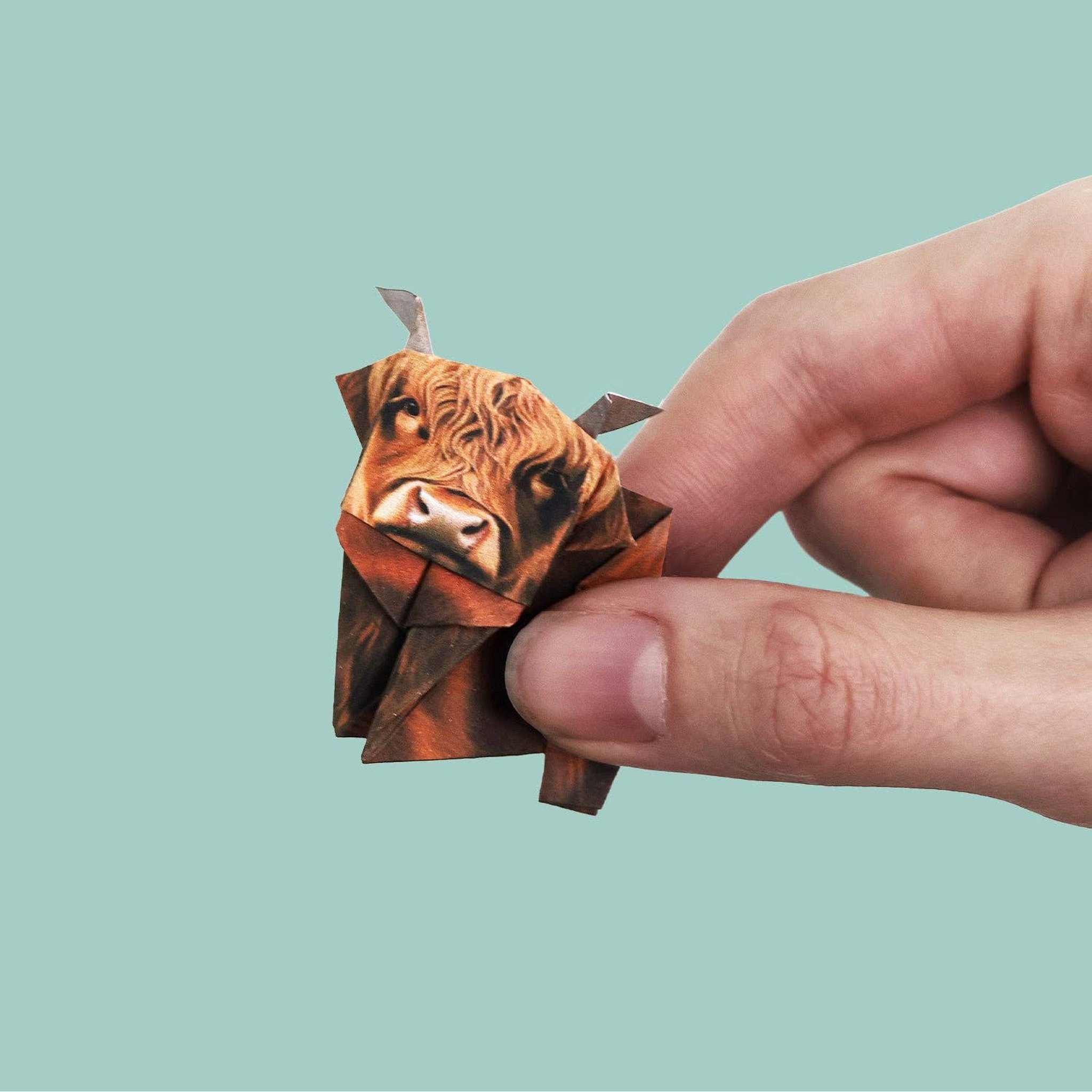 Fingers holding a small folded origami Highland cow