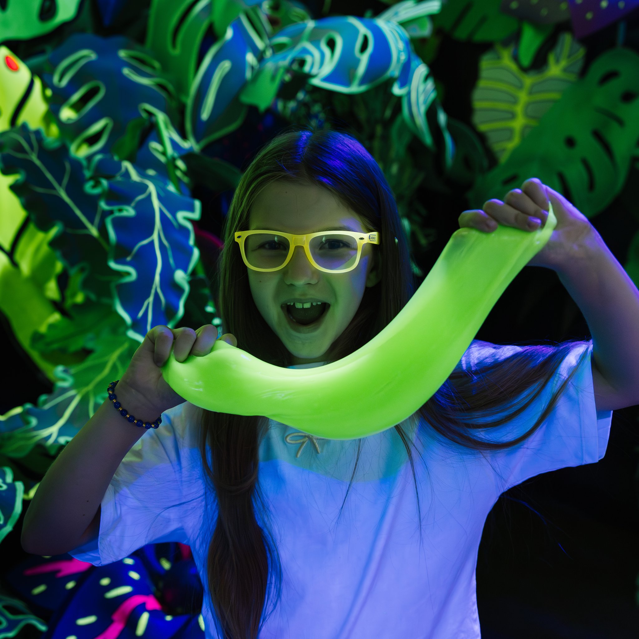 Ragazza con occhiali che allunga lo slime verde fluorescente sotto la luce nera