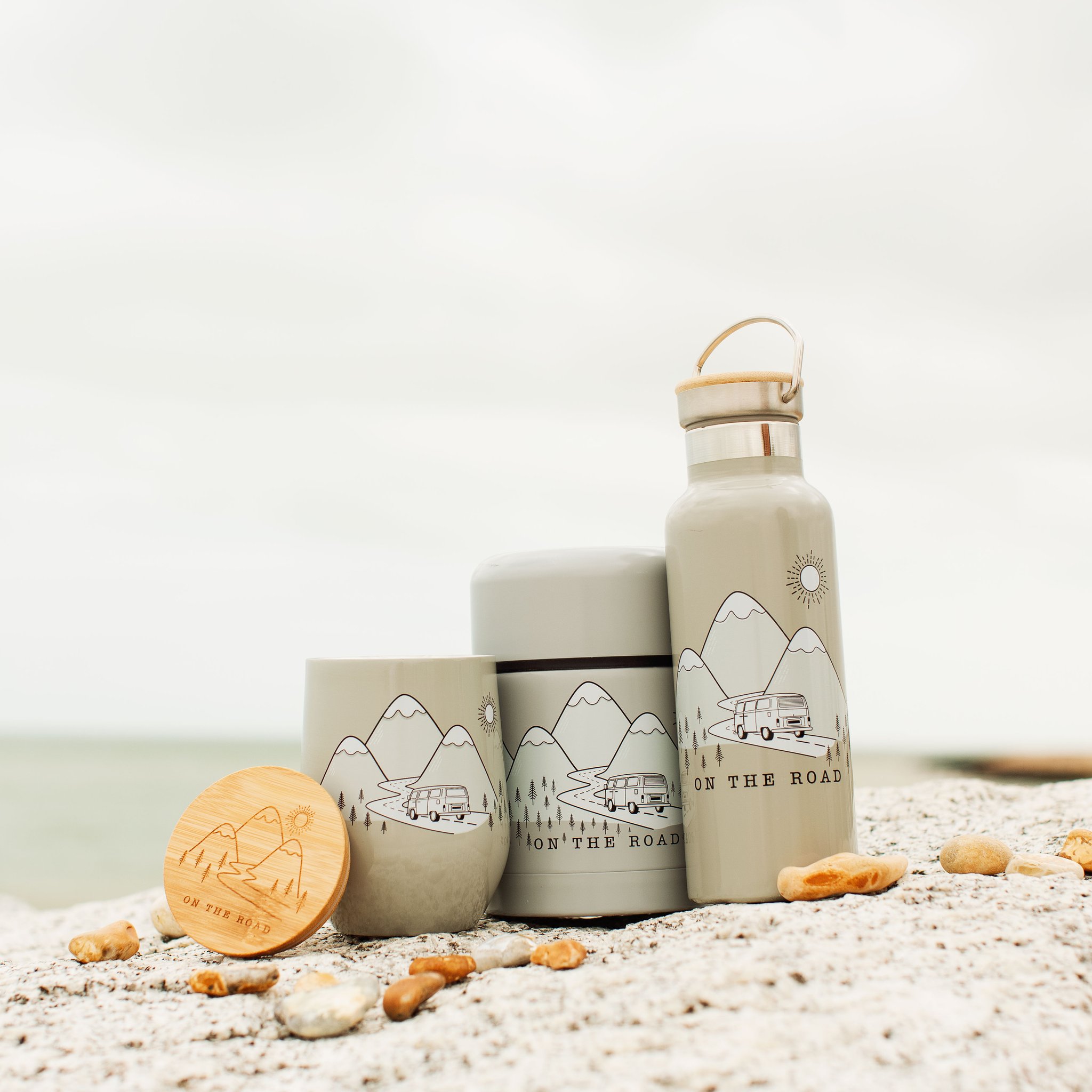 Mug On the Road avec la boîte isotherme et la gourde de la série sur des rochers au bord de la mer