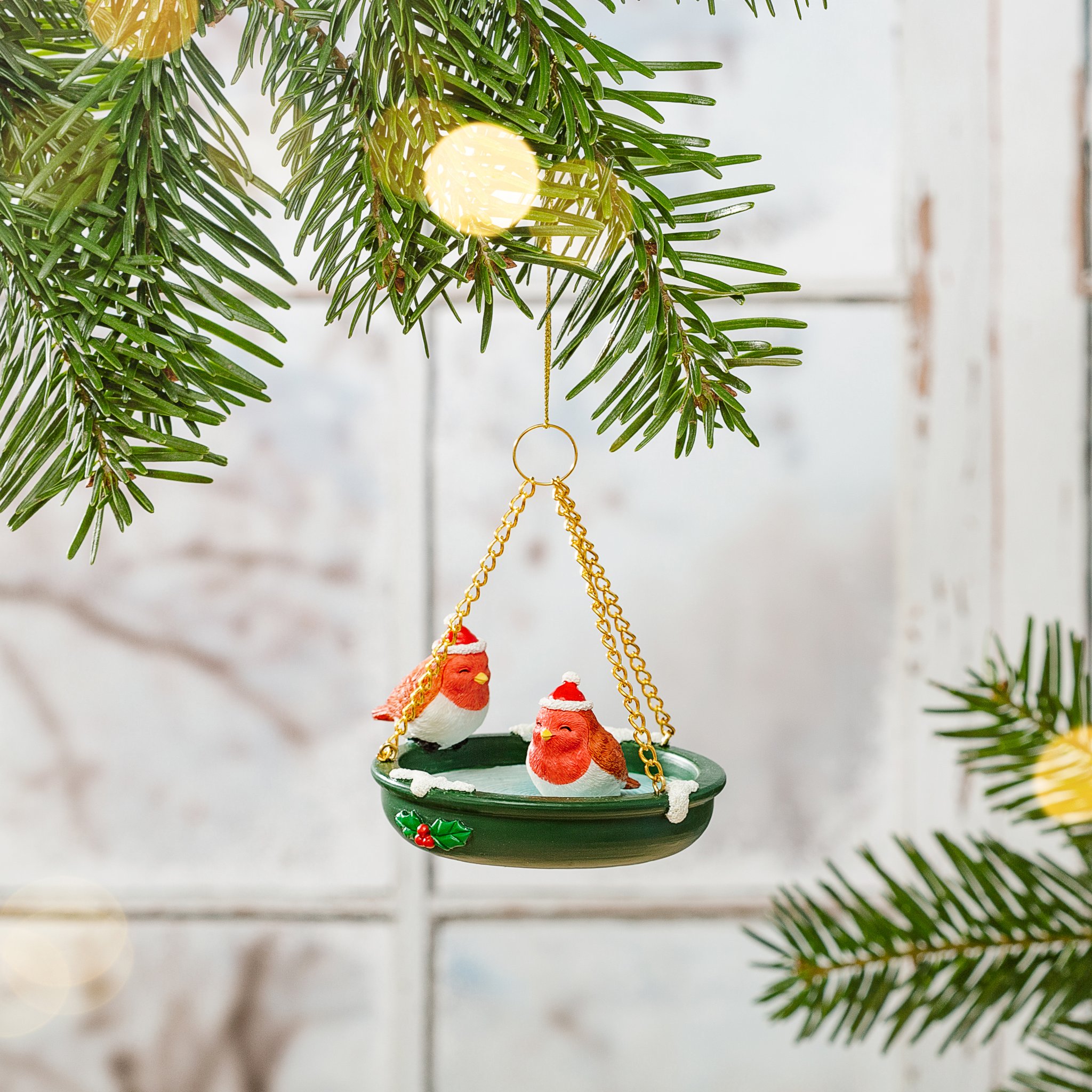 Décoration de Noël bain d'oiseaux suspendue à une branche de sapin devant une fenêtre claire