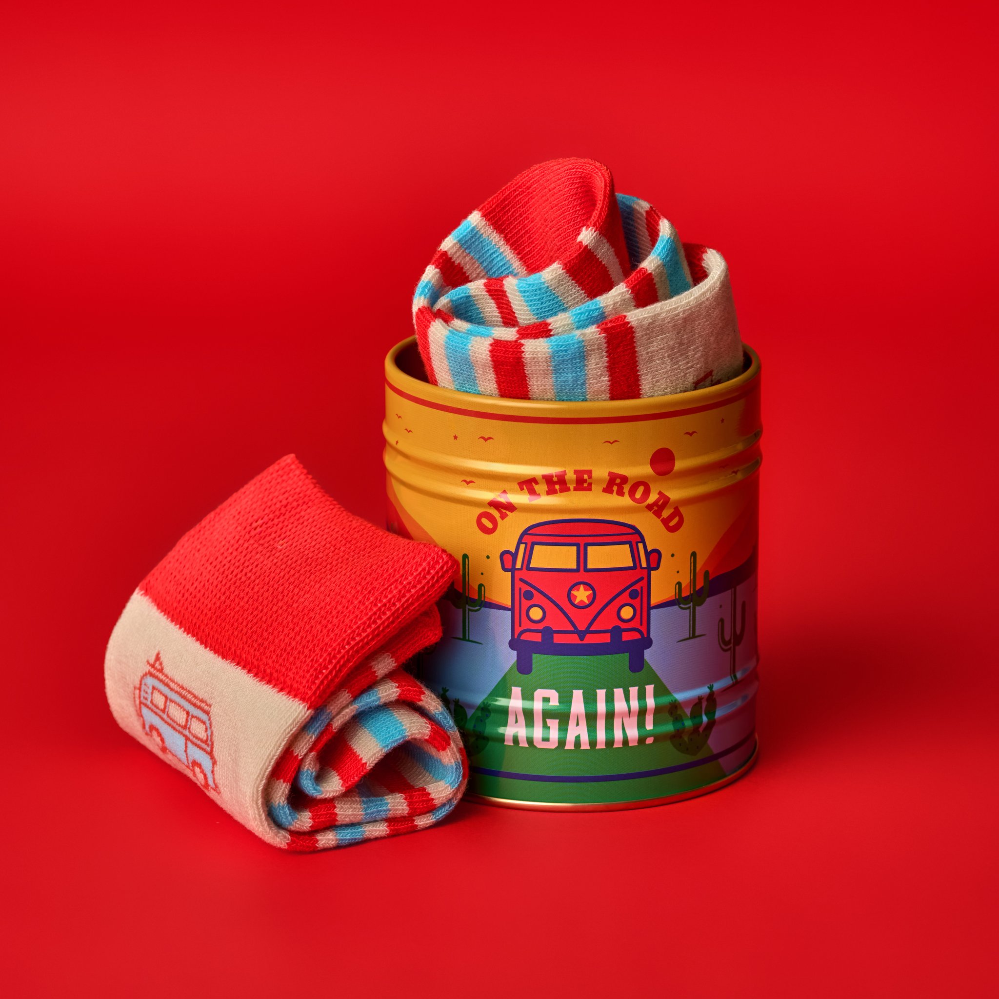 Boîte du set de chaussettes Camping sur fond rouge, une chaussette roulée à côté et d'autres qui dépassent