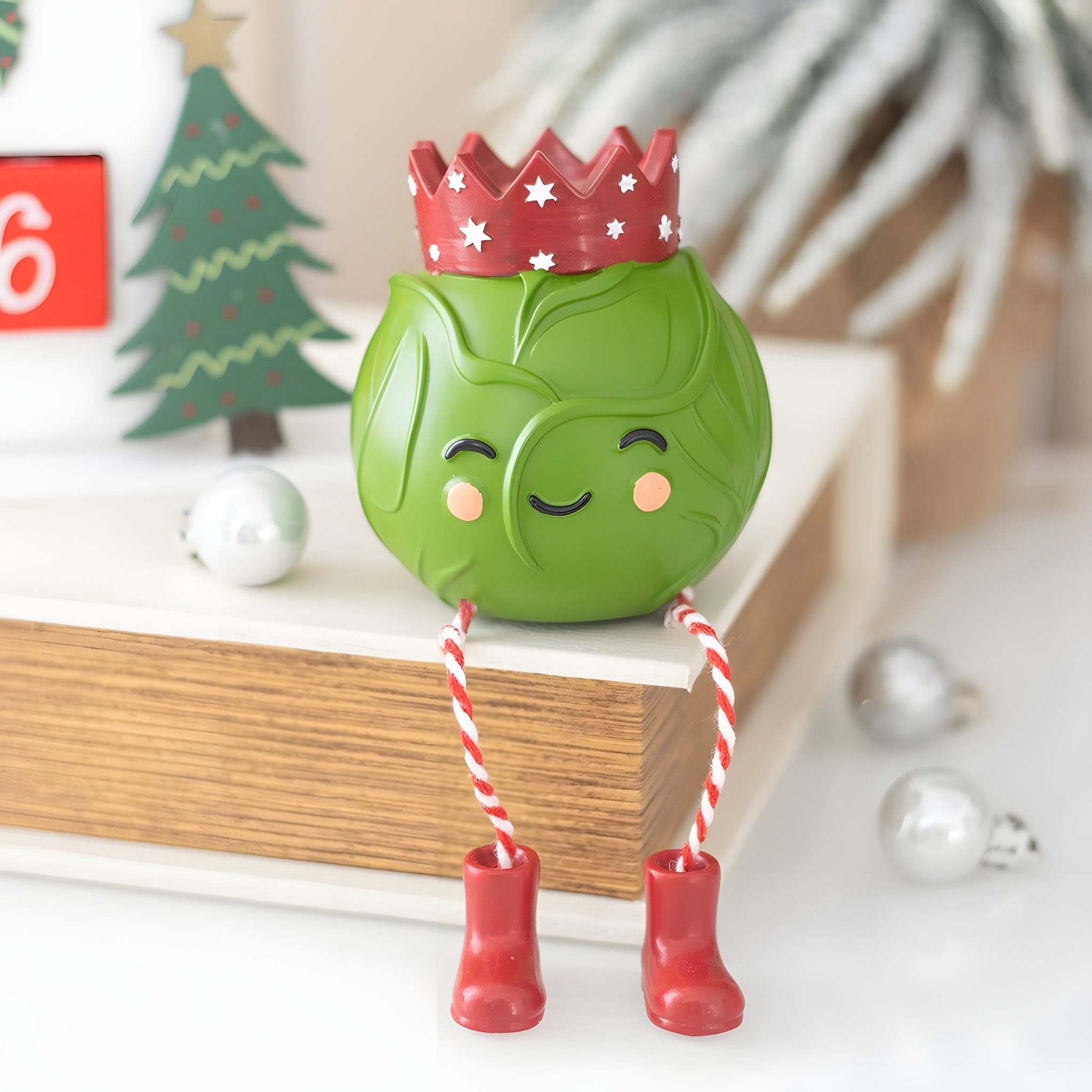 Chou de Bruxelles à poser avec couronne assis sur un livre parmi la déco de Noël