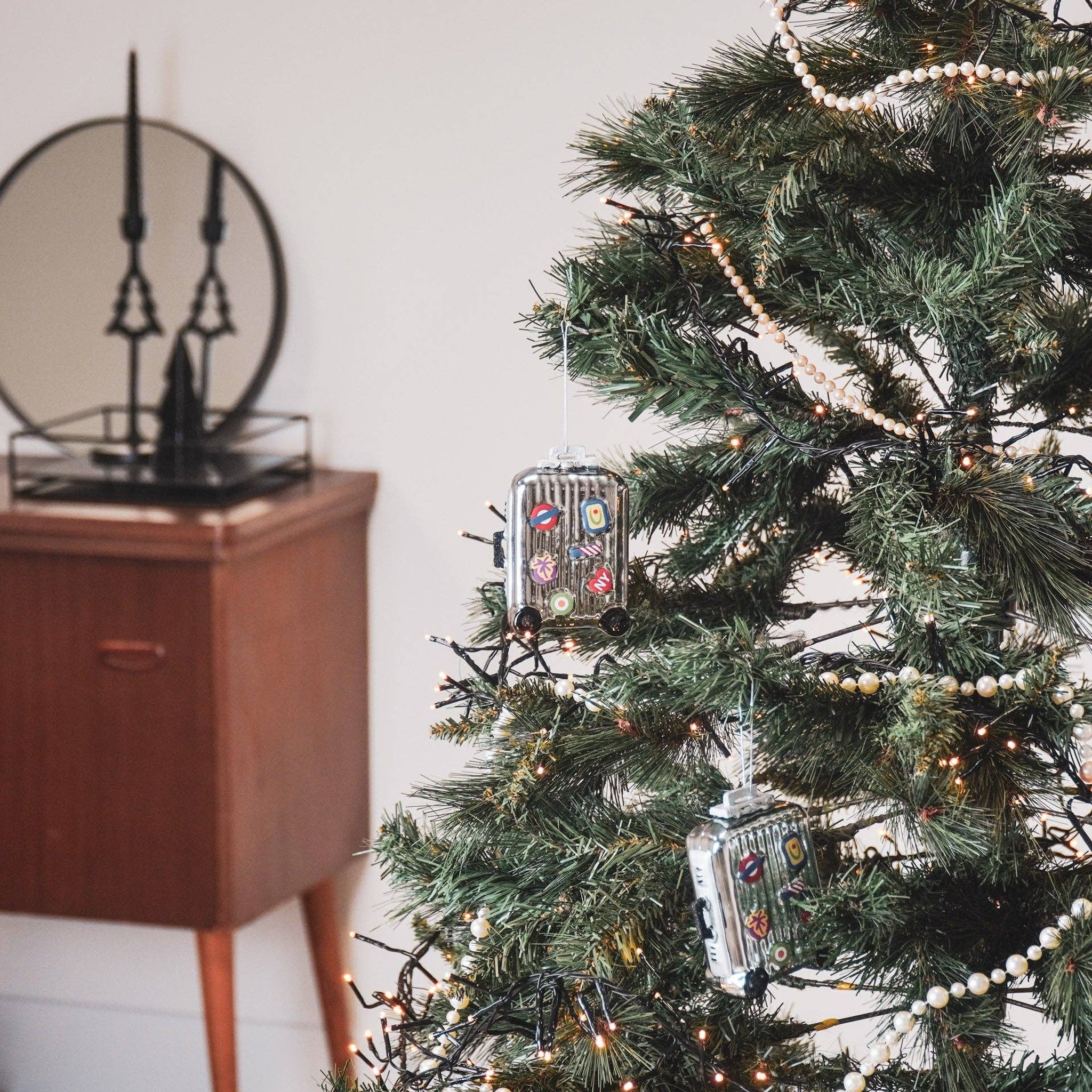 Zwei Koffer Weihnachtsanhänger mit Reise-Stickern hängen an einem Weihnachtsbaum