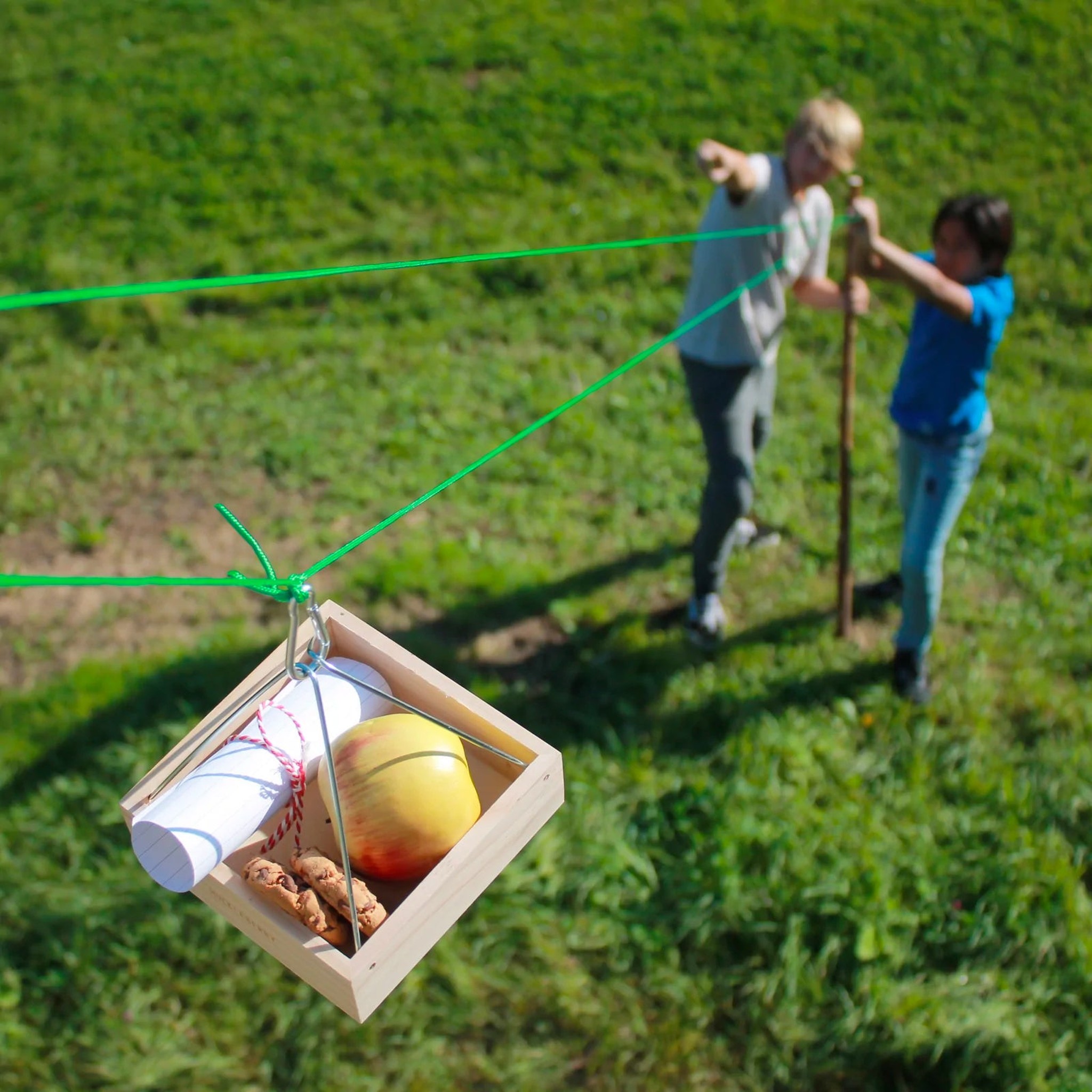 Zwei Kinder spielen mit Huckleberry Seilbahn im Garten — Gondel gleitet auf grünem Seil