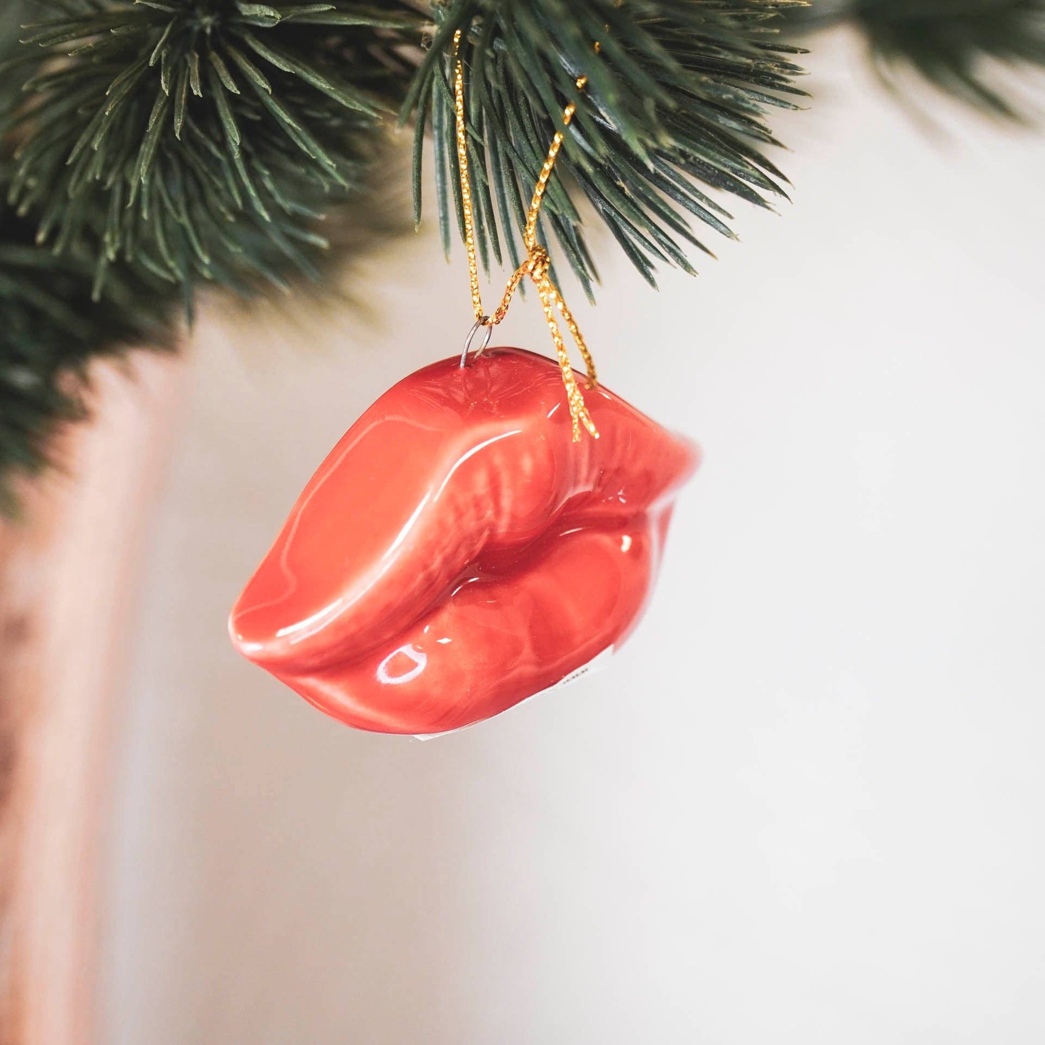 Rote Lippen Weihnachtsanhänger aus Keramik hängt nah an einem Tannenzweig