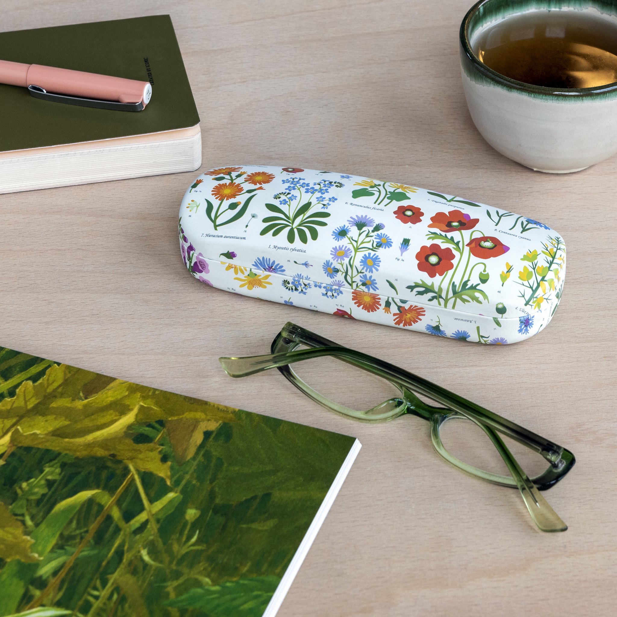 Astuccio per occhiali fiori di campo sul tavolo accanto a occhiali, taccuino e una tazza di tè