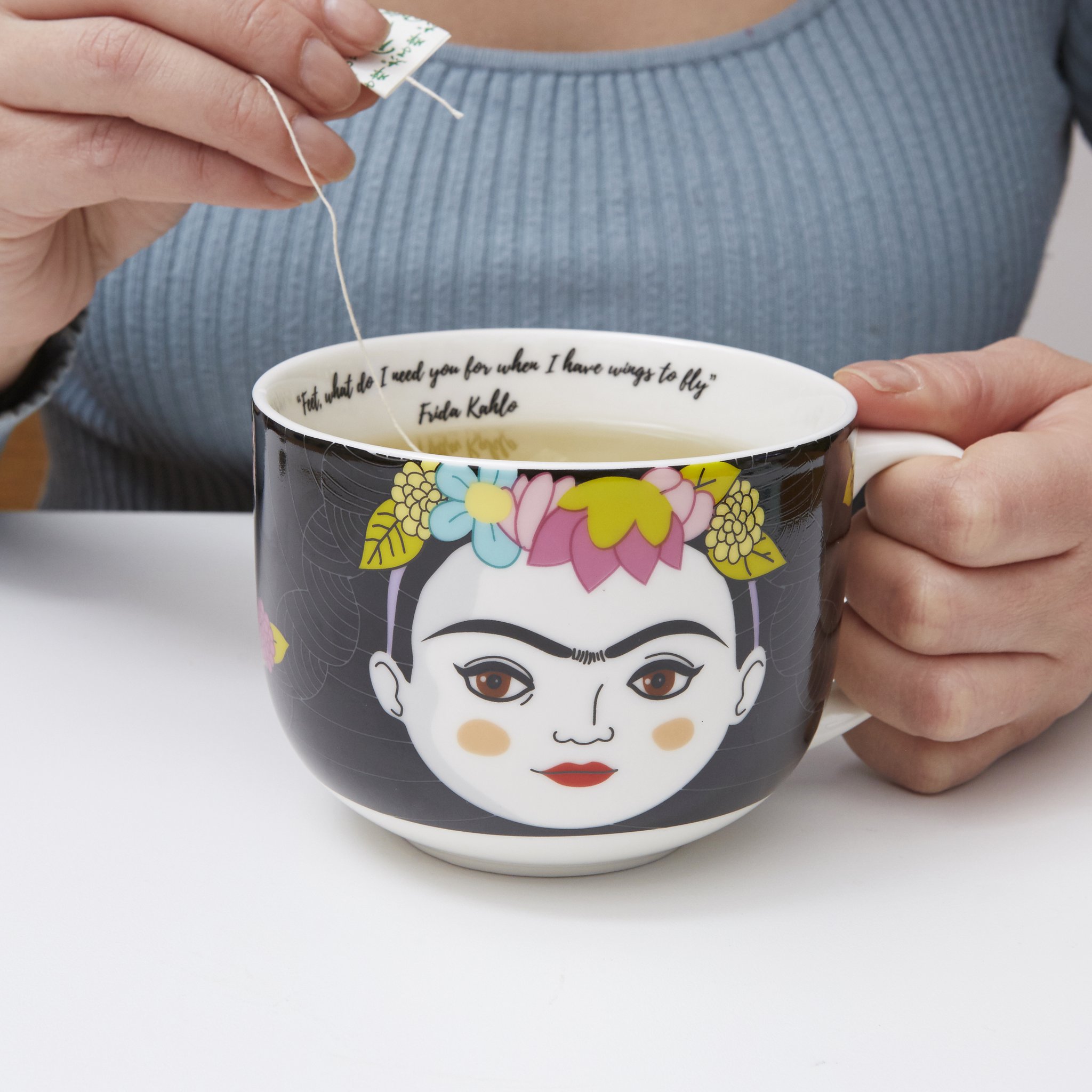 Mains tenant le mug Frida avec du thé, sachet retiré