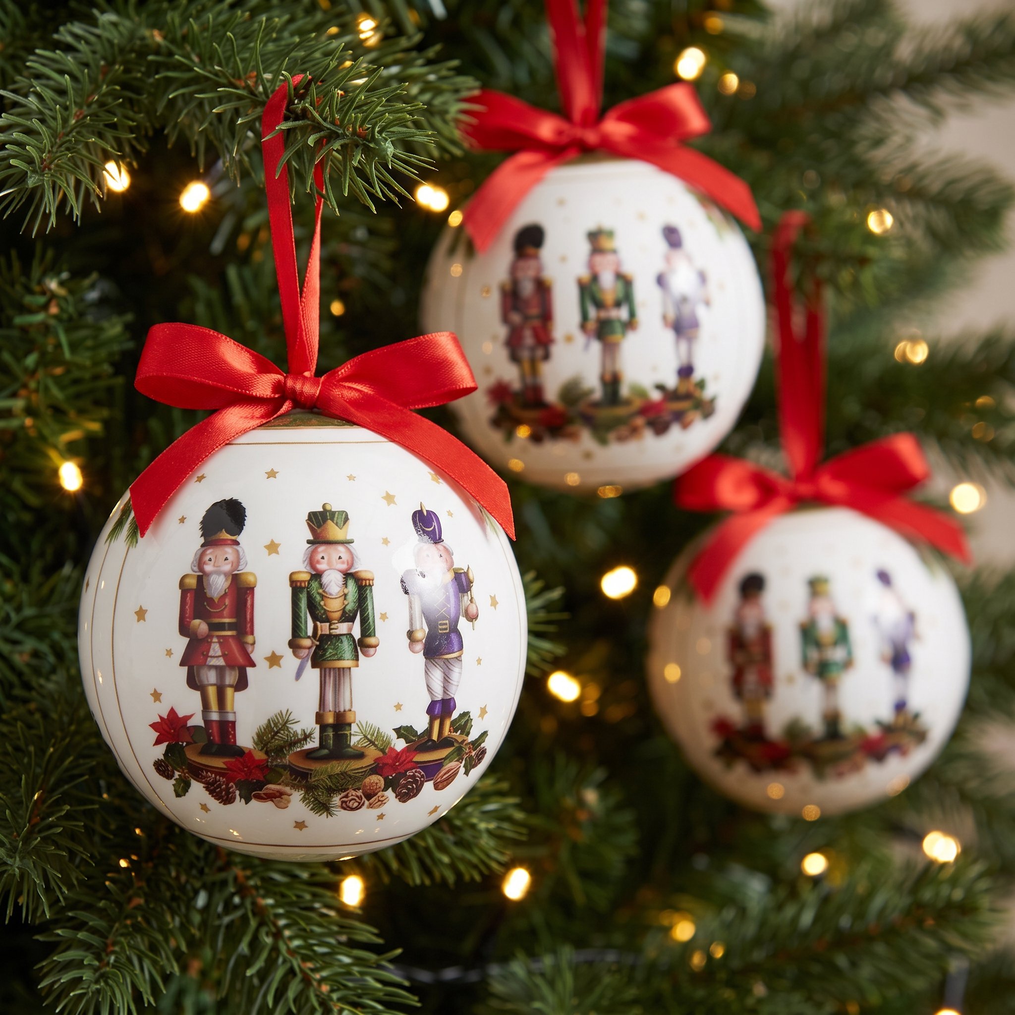Three nutcracker Christmas baubles with red bows in the Christmas tree against warm fairy lights