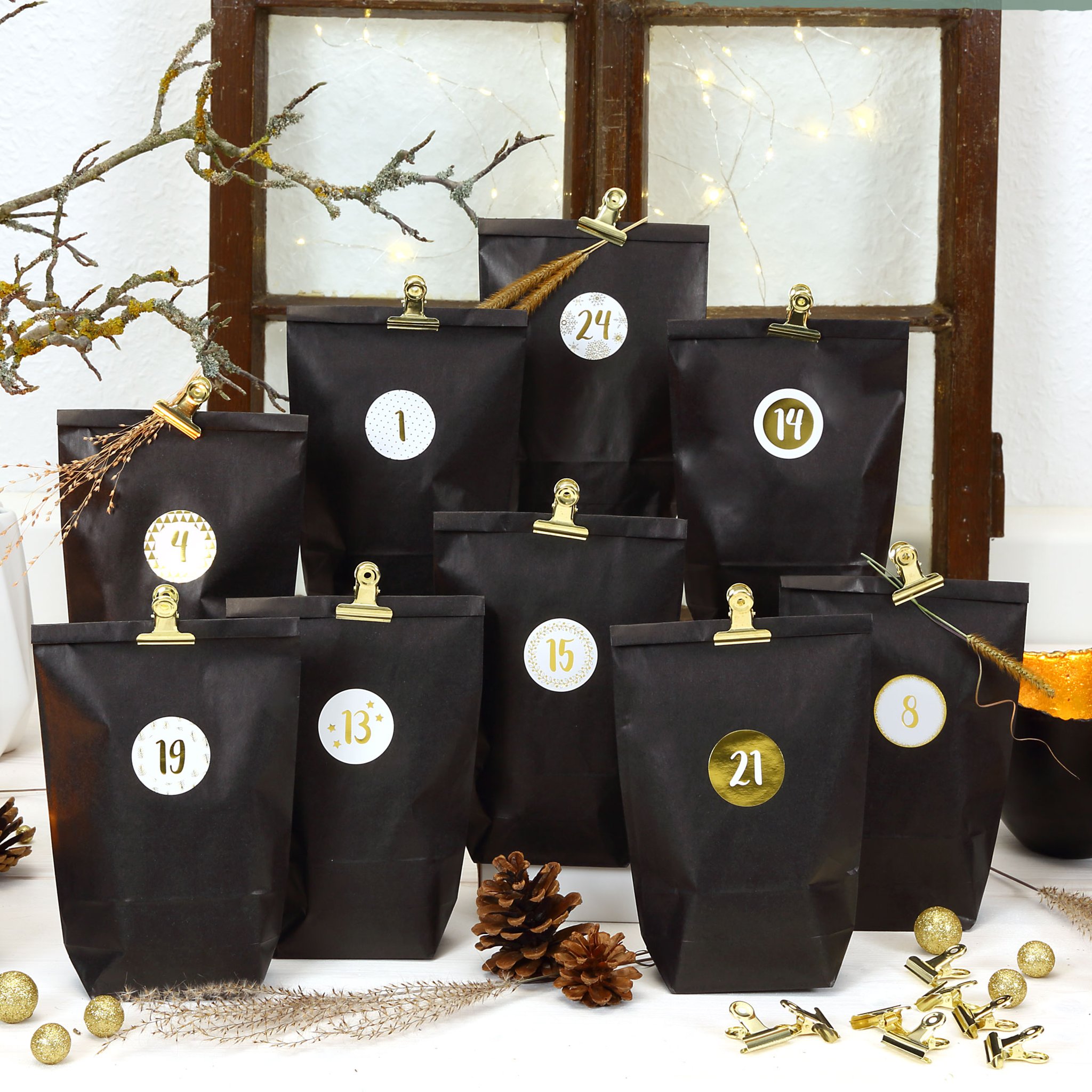 Adventskalender Elegance: schwarze Beutel mit goldenen Metallklammern und Zahlen vor einem alten Fenster