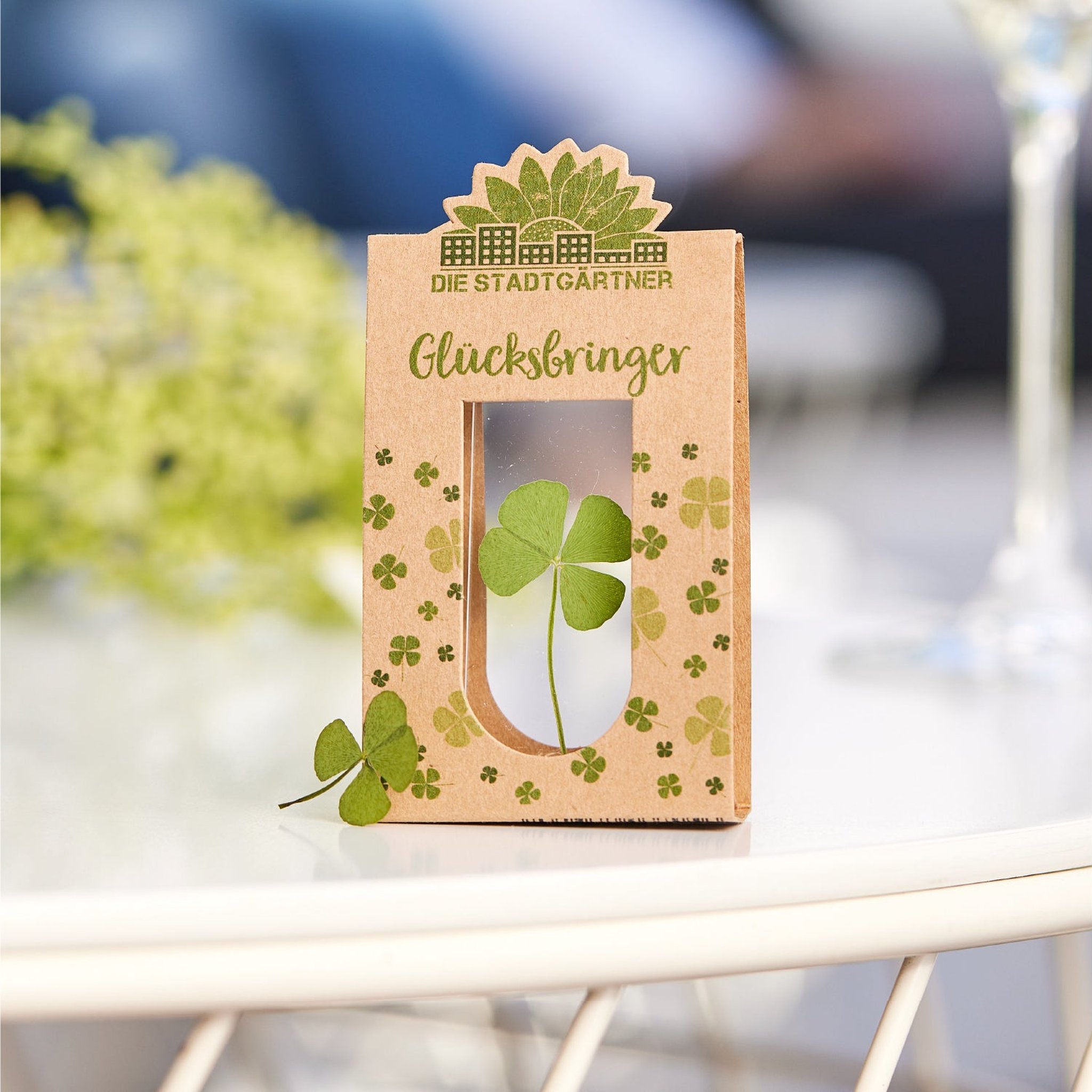 Glücksbringer auf einem weissen Gartentisch im Freien, daneben ein einzelnes Kleeblatt