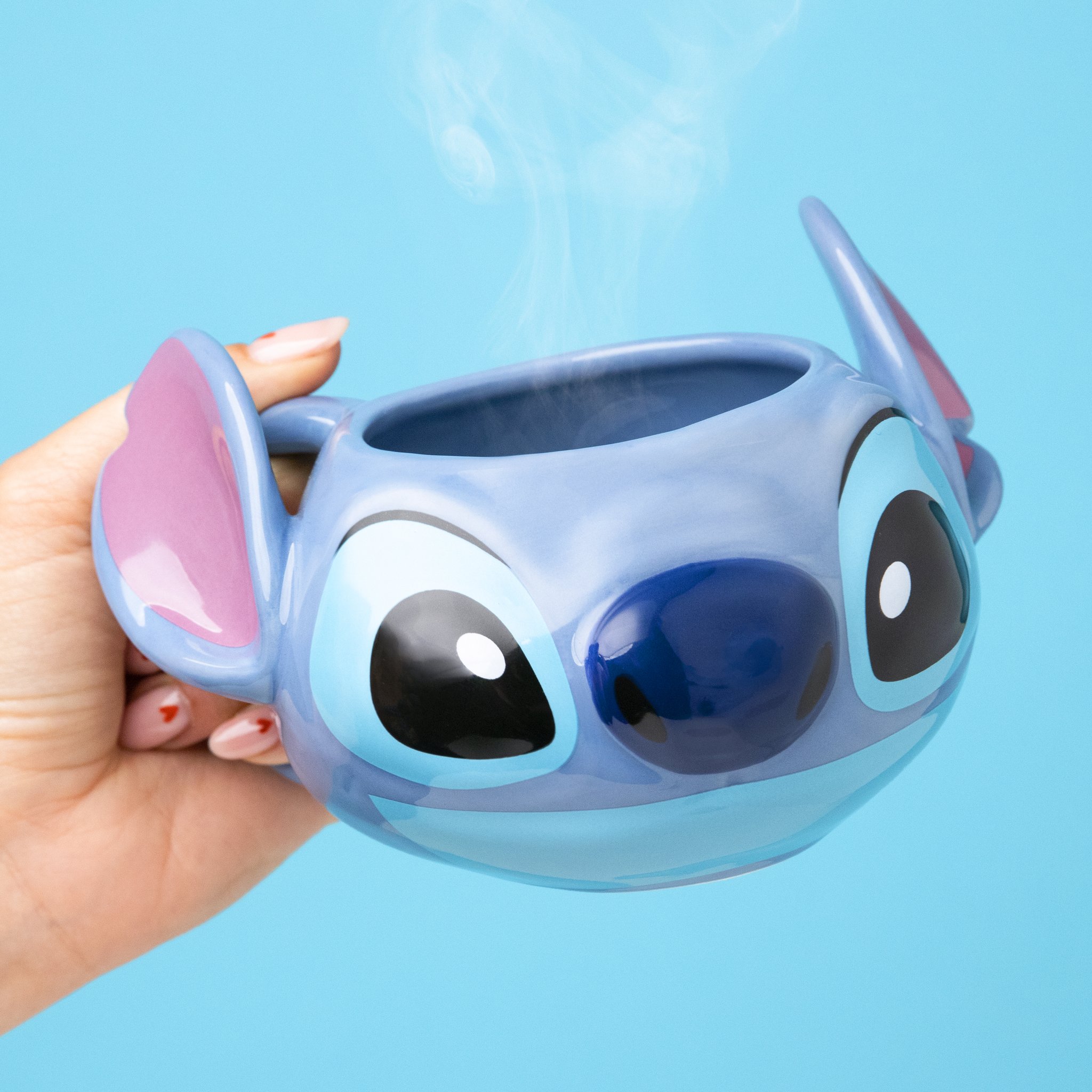 Hand hält die Stitch-Tasse seitlich vor hellblauem Hintergrund
