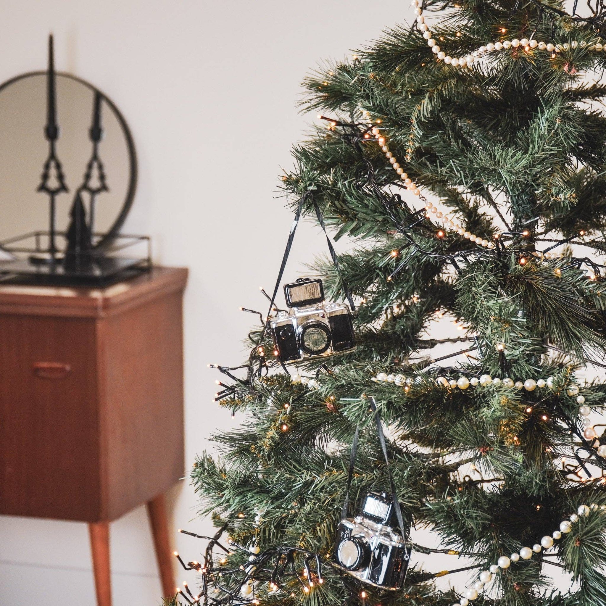 Retro-Kamera Weihnachtsanhänger aus Glas hängt an einem geschmückten Tannenzweig