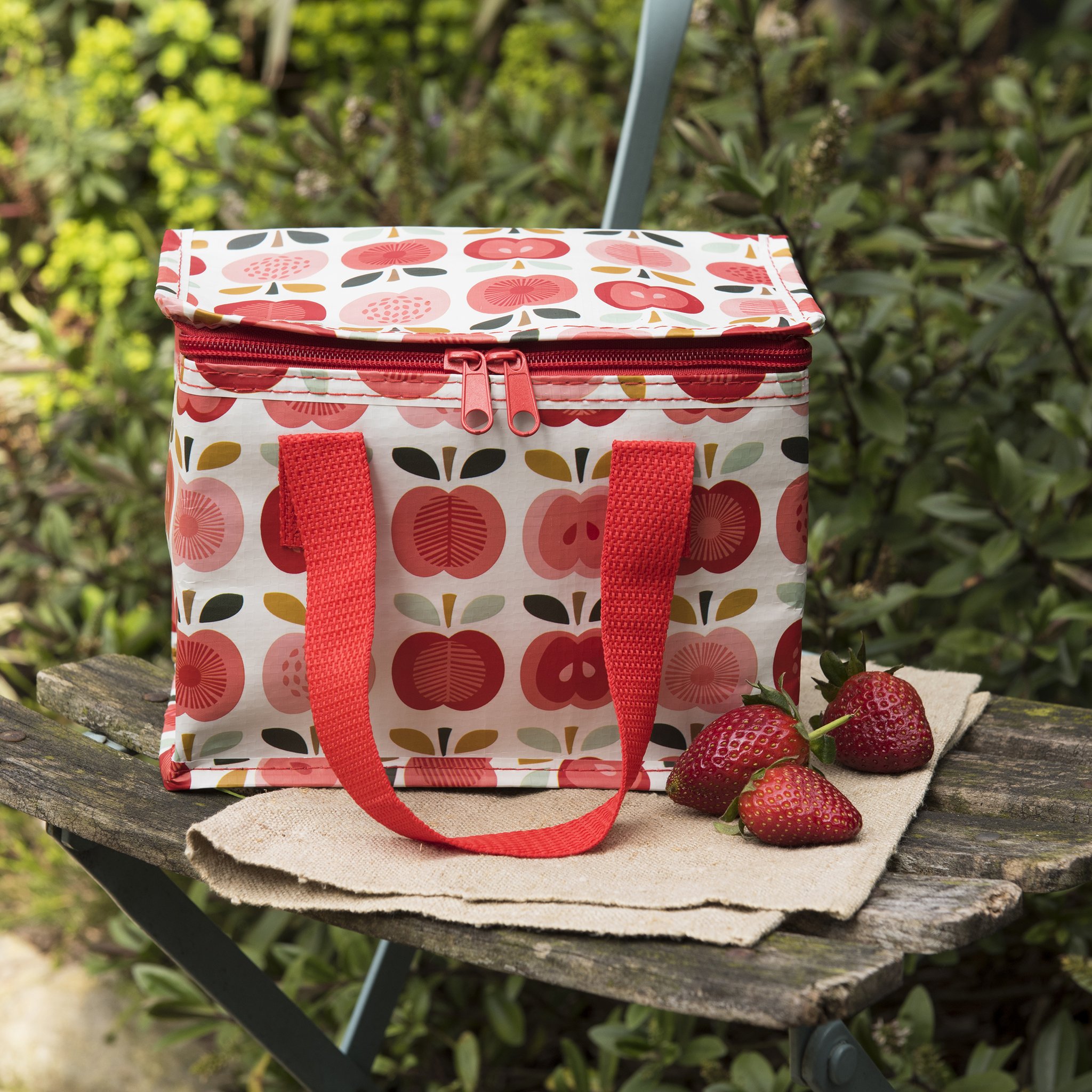 Apfel-Kühltasche auf einem Gartenstuhl mit Erdbeeren im Grünen