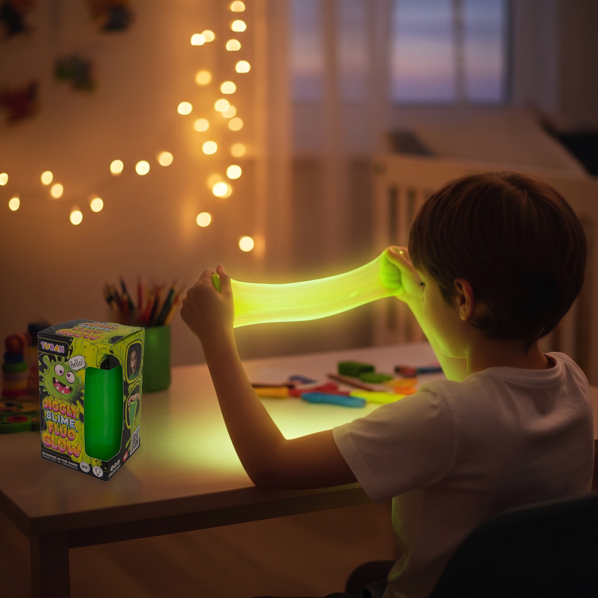 Bambino che allunga lo slime Jiggly verde luminoso nella cameretta di sera, scatola Tuban accanto