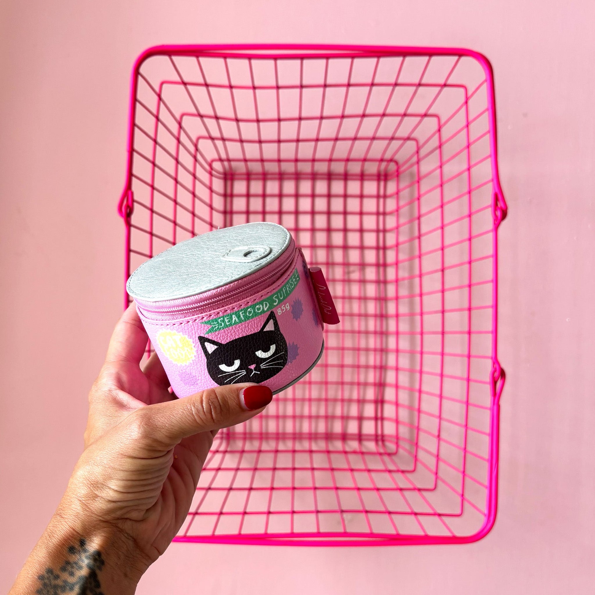 Hand holding the cat food tin storage case in front of a pink wire basket