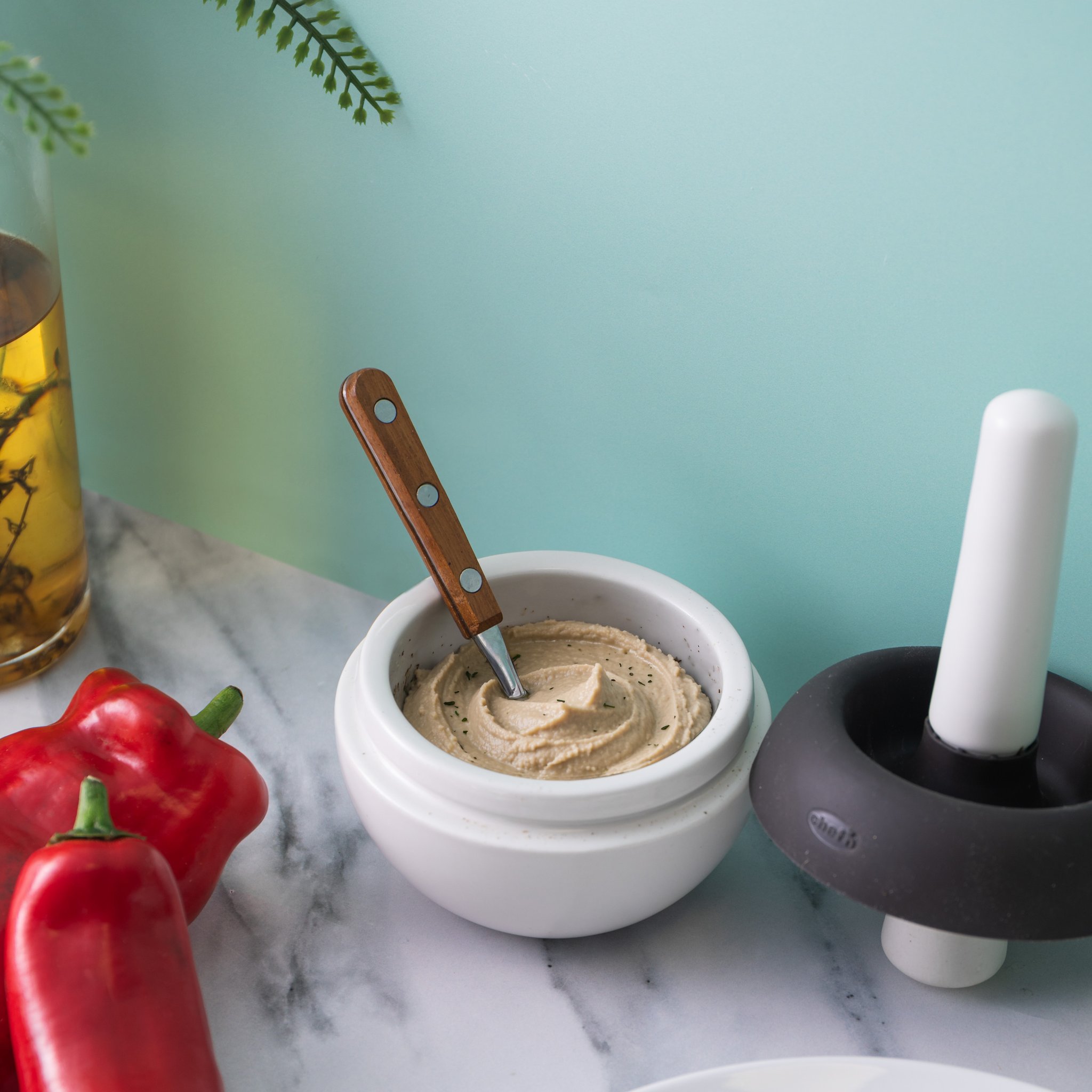 Mörserschale mit Hummus und Messer, daneben Spritzschutz und Stössel