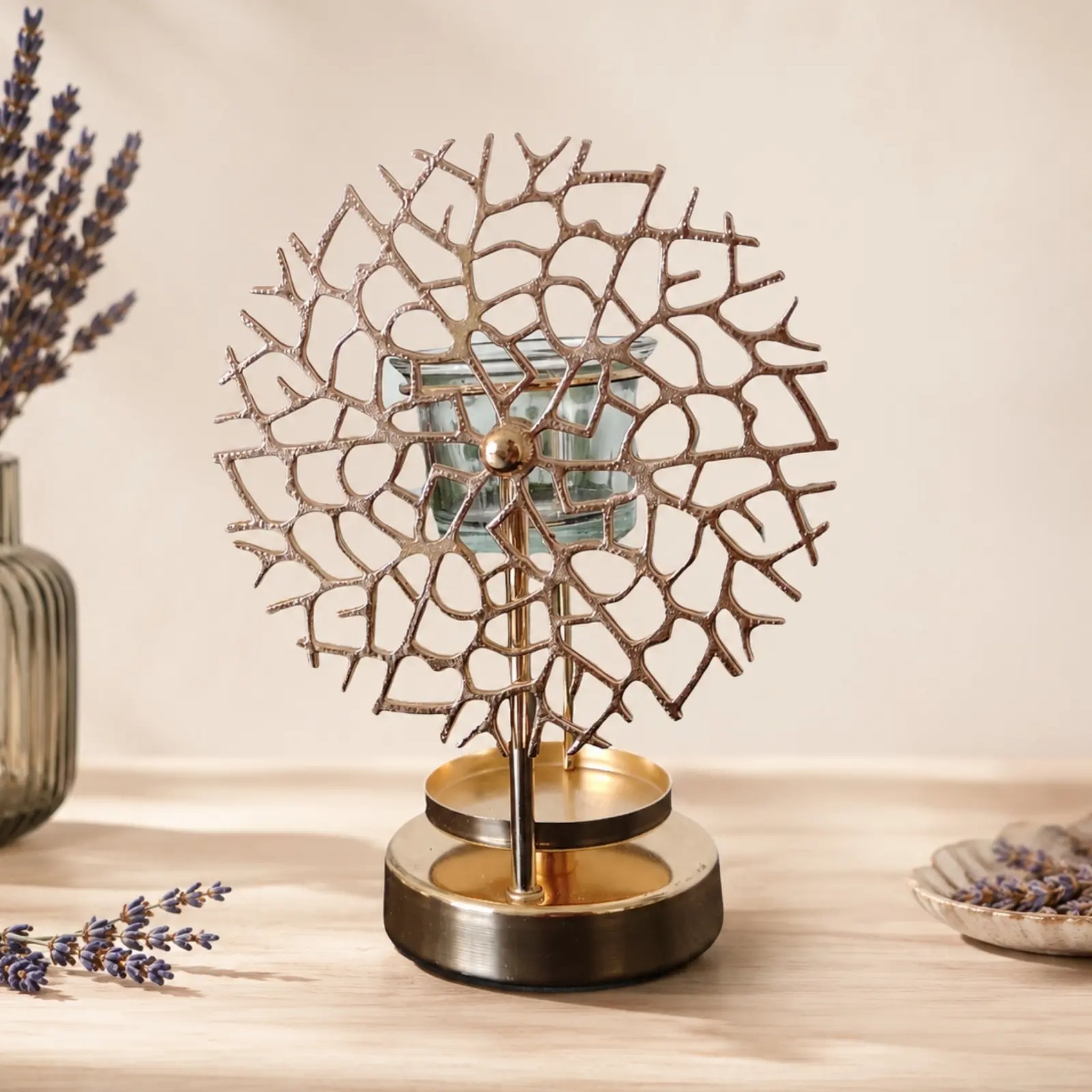 Gold-coloured oil burner with round coral pattern and glass cup beside lavender