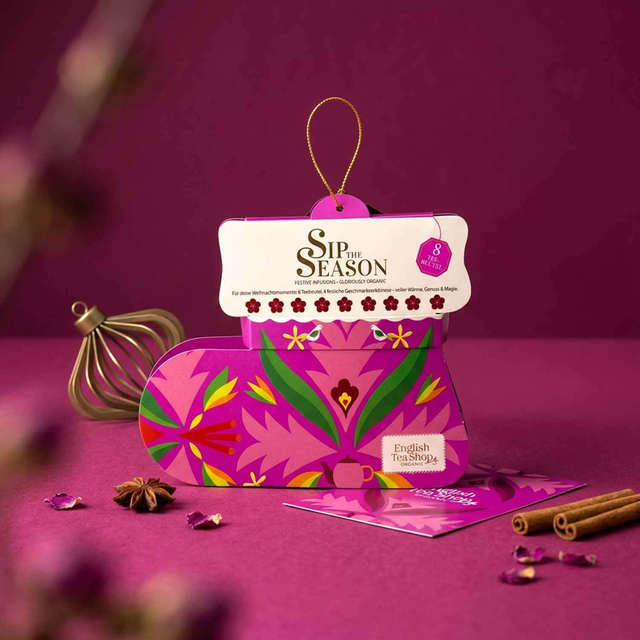 Botte de Noël rose garnie de thé sur fond framboise avec anis étoilé, cannelle et boule de Noël