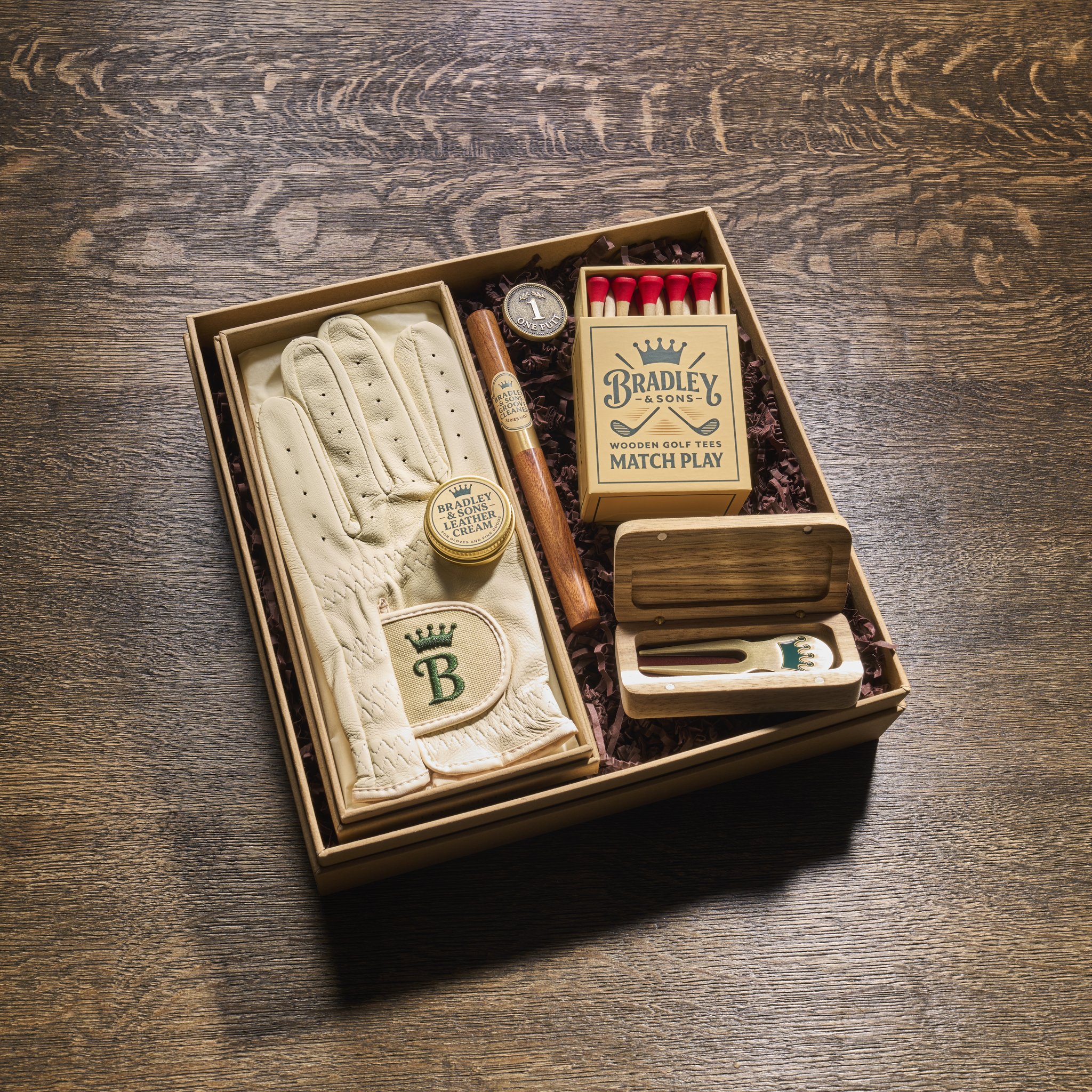 Innenansicht der Golf-Geschenkbox: Handschuh, Ballmarker, Tee-Schachtel und Divot-Tool auf Holzwolle
