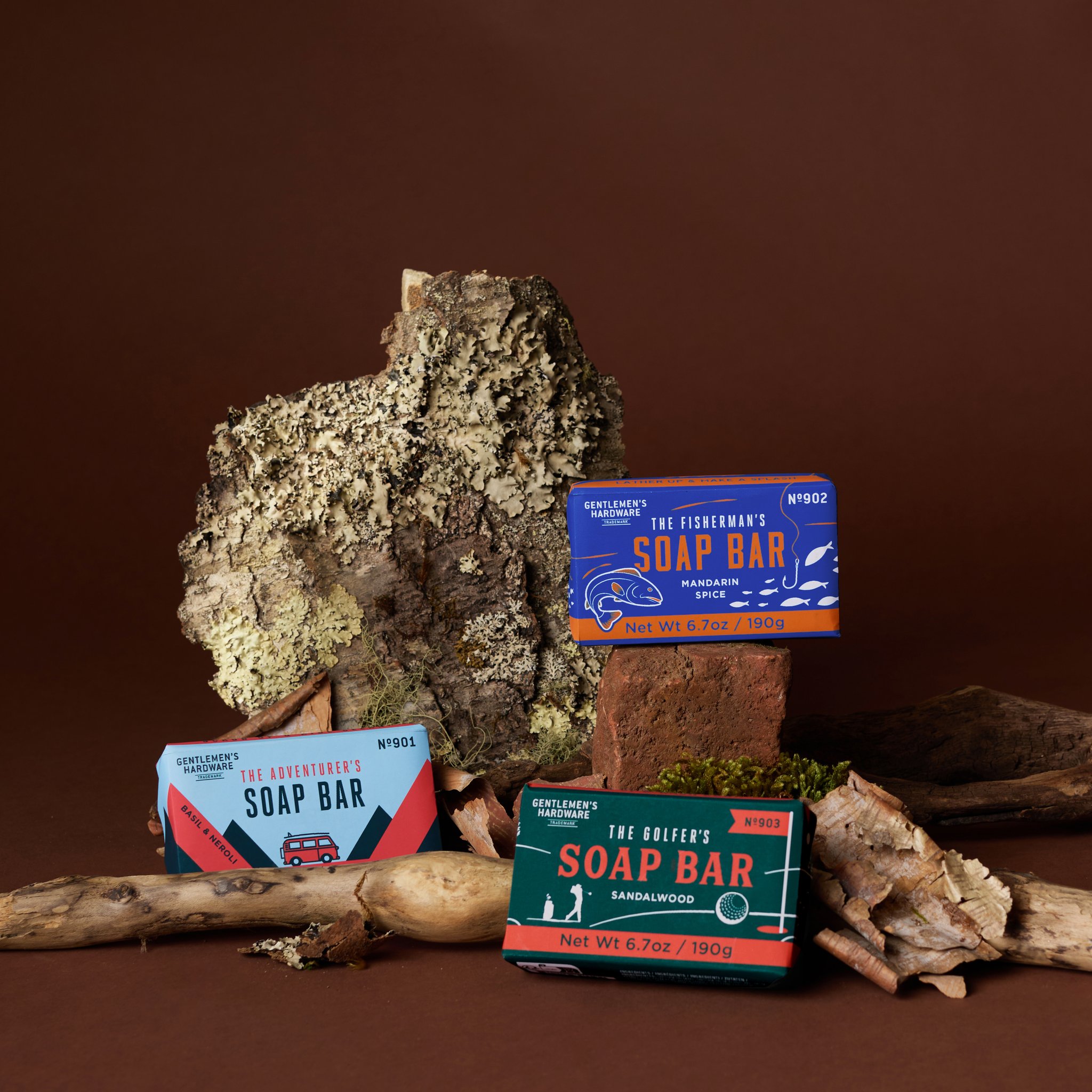 Abenteurer-Seife und zwei weitere Seifen auf Holz und Rinde, die Verpackung der Abenteurer-Seife links