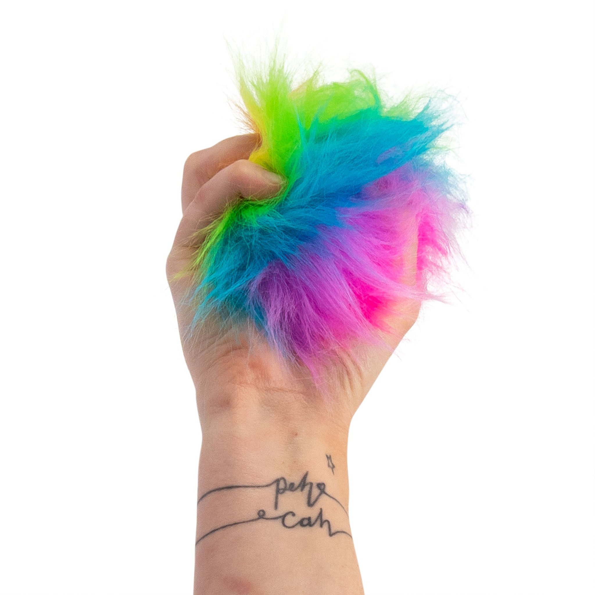 Hand drückt den Scrunchems Furry Sugar Squish Ball mit Regenbogenfell zusammen