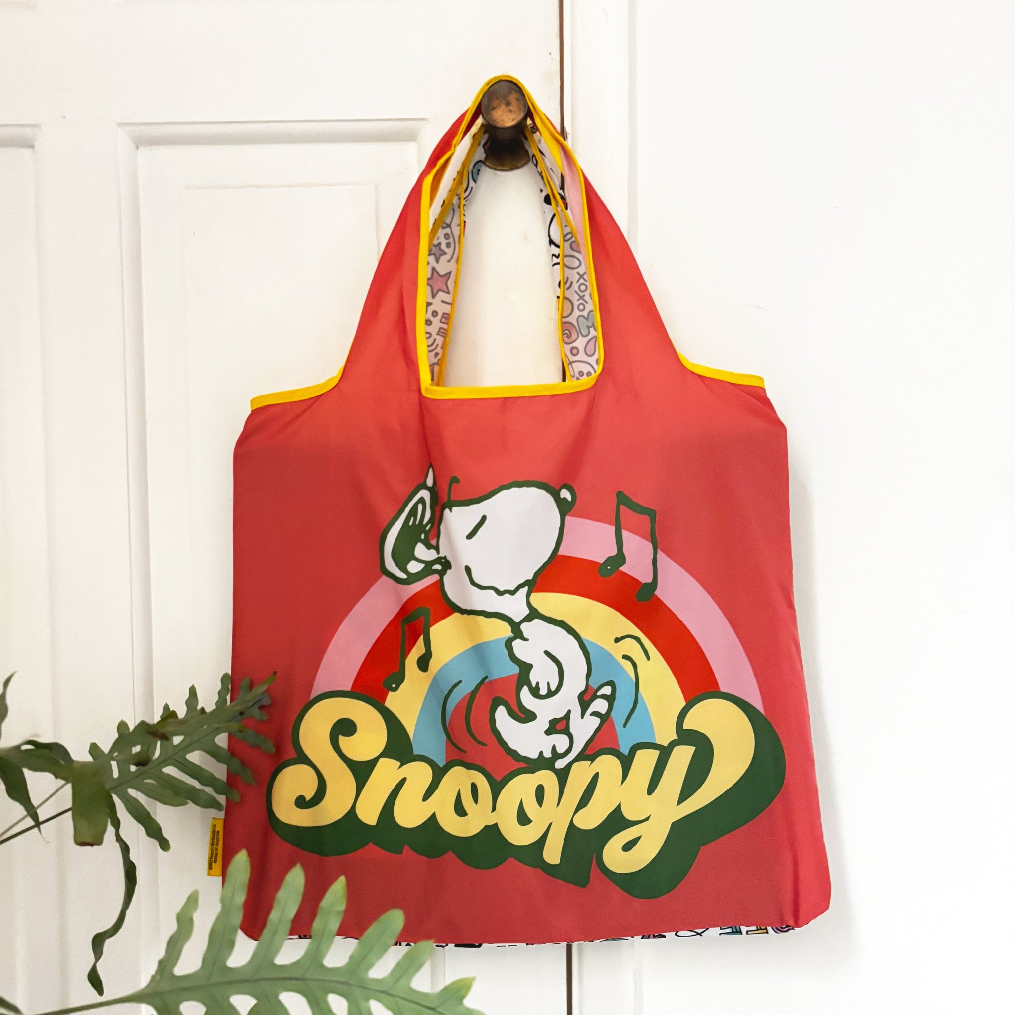 Red Peanuts shopping bag with Snoopy on a rainbow hanging from a door hook