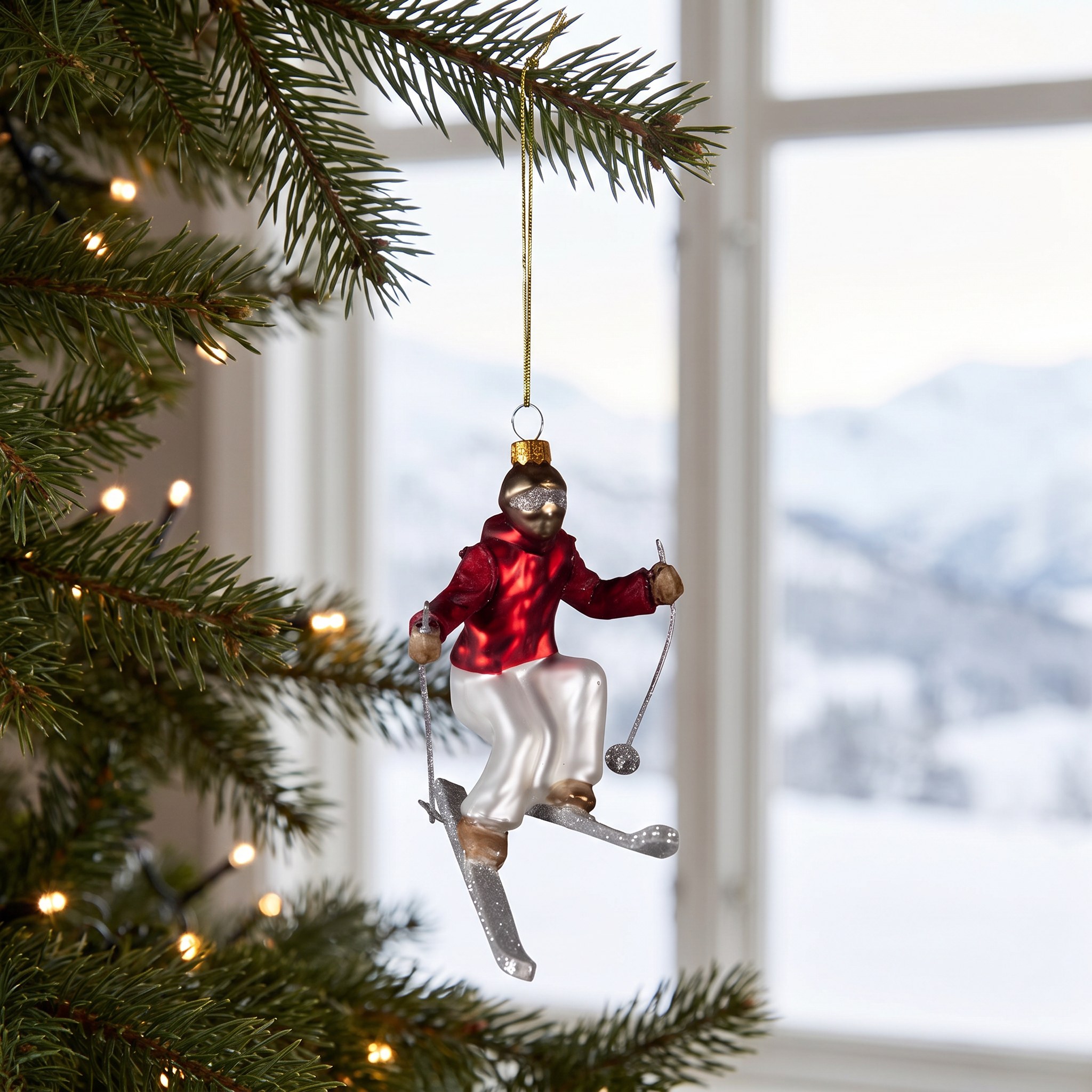Skifahrer aus Glas hängt am Weihnachtsbaum vor einem Fenster mit verschneiten Bergen