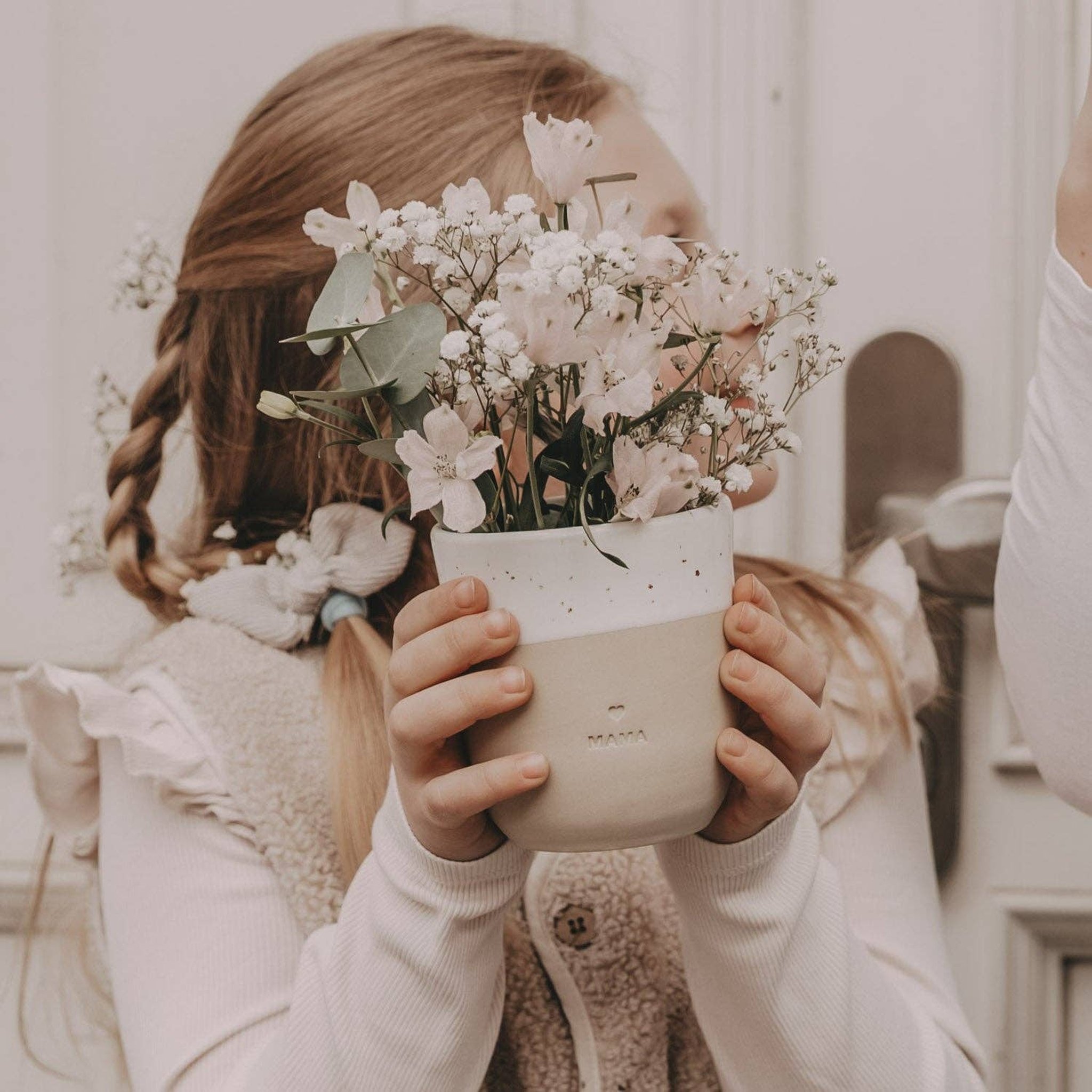 Mädchen hält den Becher Mama mit einem Strauss weisser Blumen in den Händen