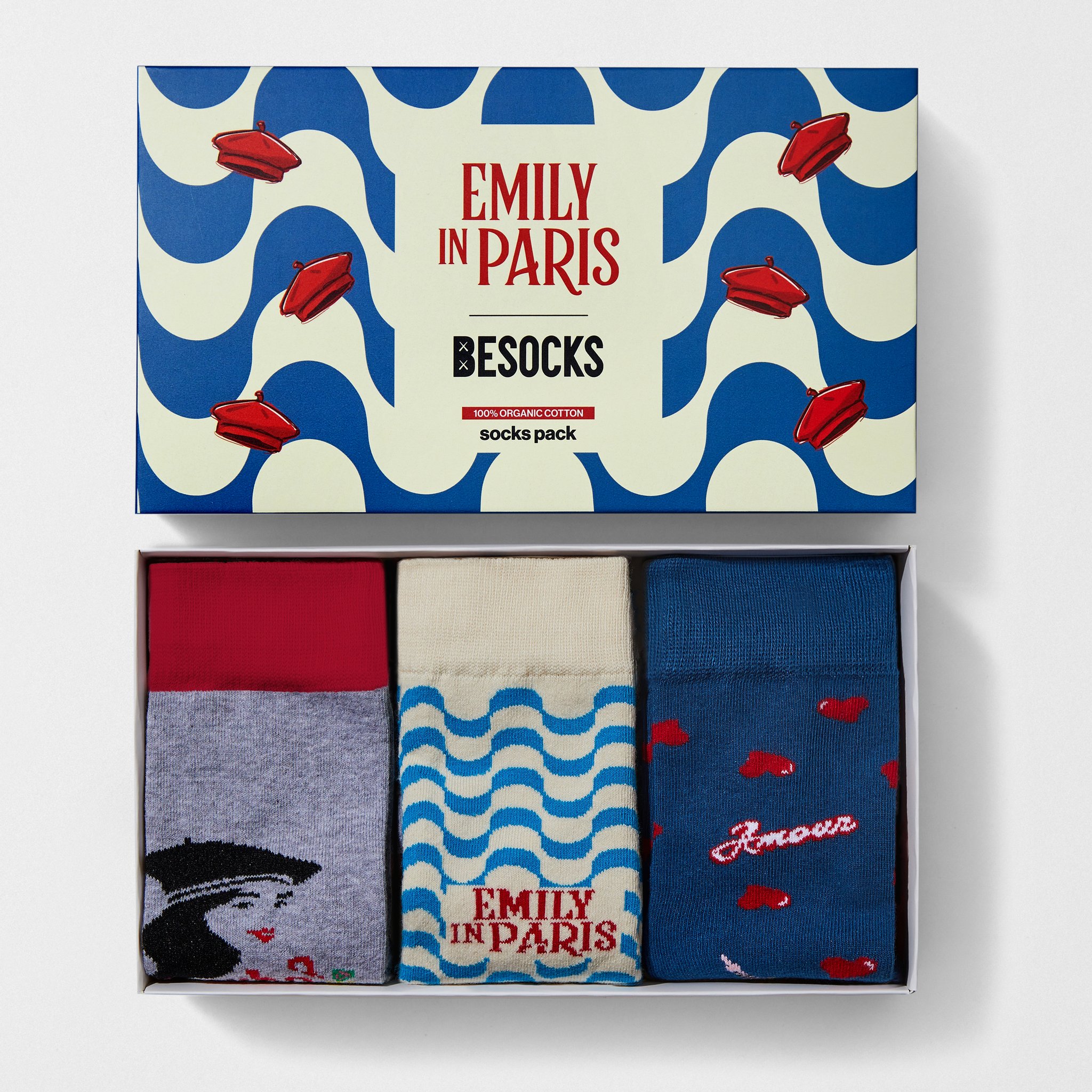 Confezione regalo Emily in Paris aperta con tre paia di calzini grigi, crema e blu