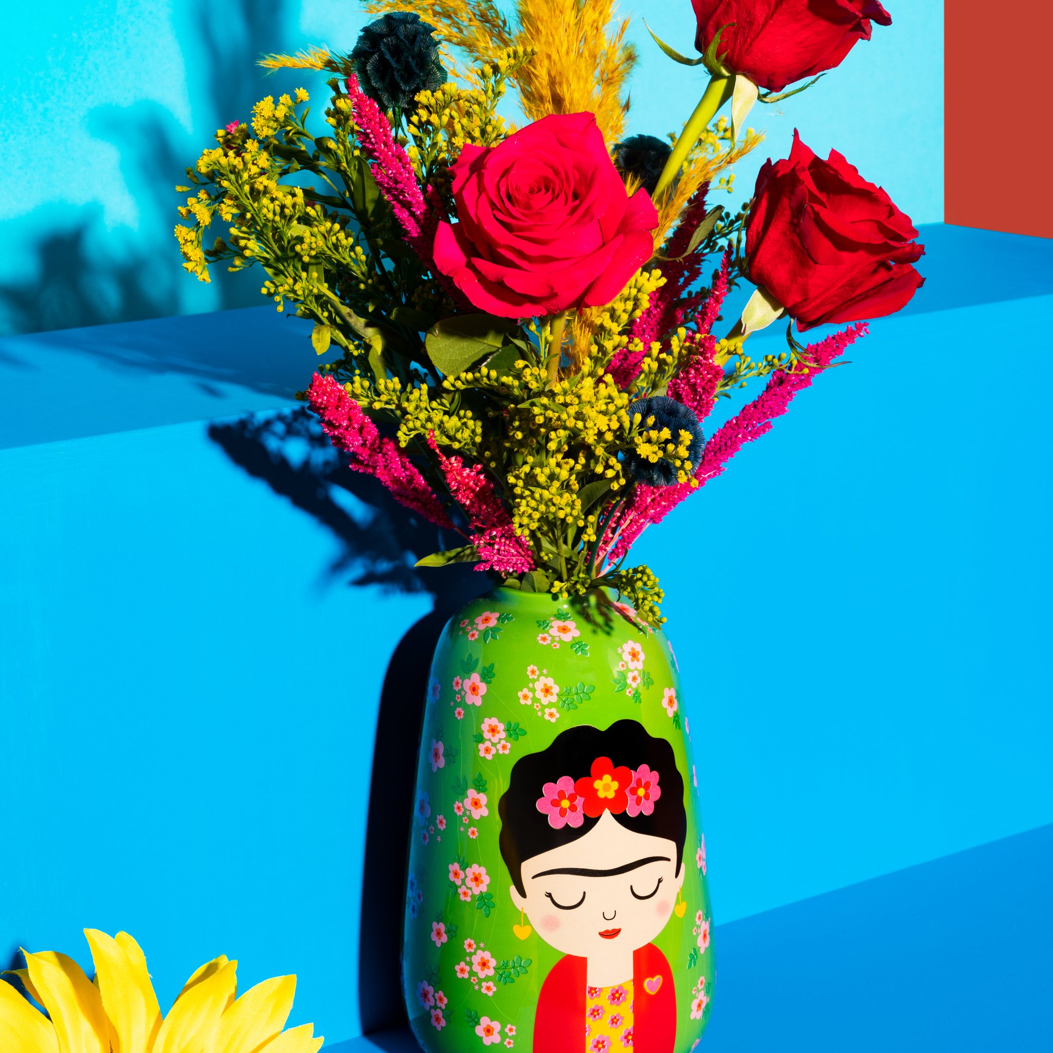 Grosse Frida Blumenvase von Sass & Belle mit Rosen und Trockenblumen vor blau-orangem Hintergrund