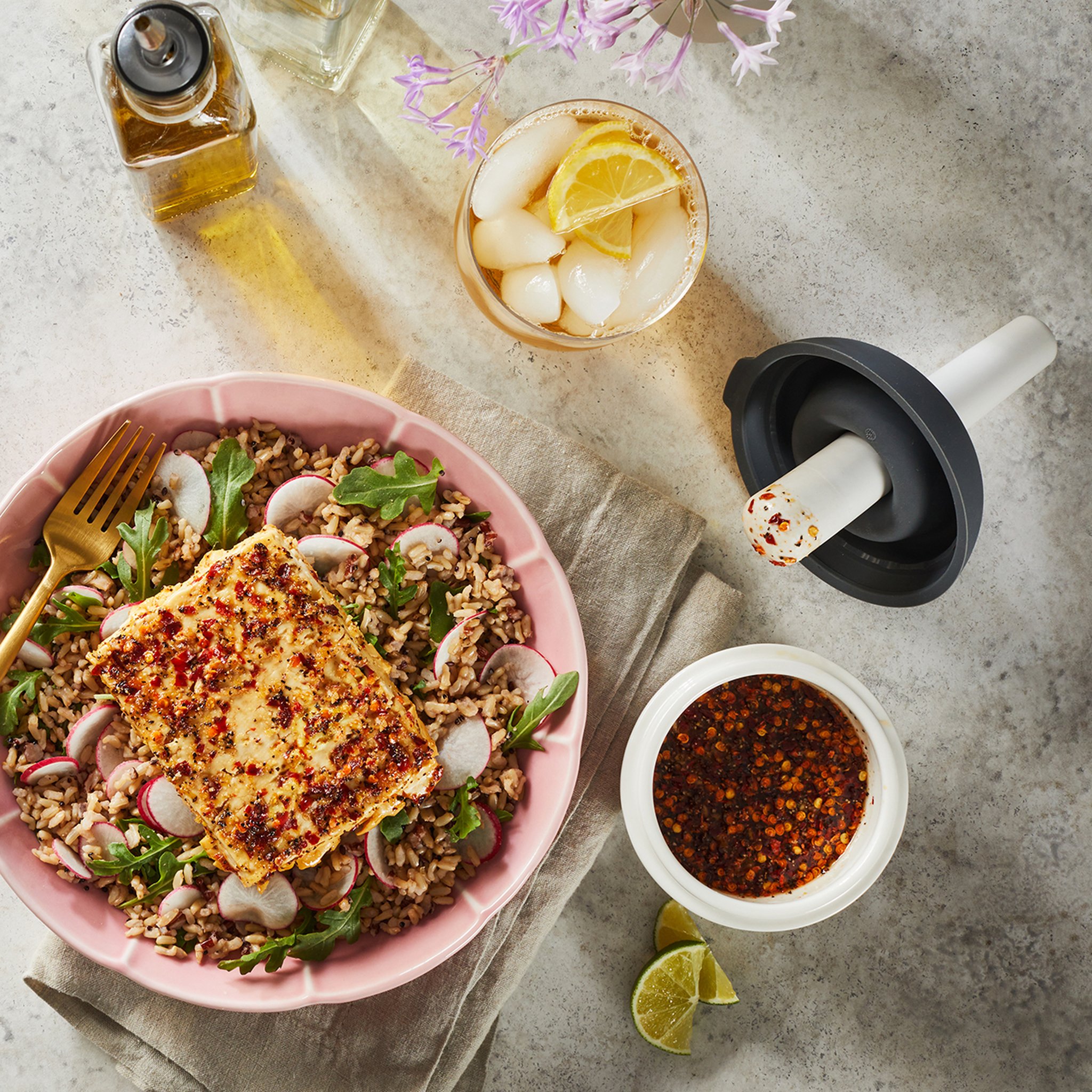 Chiliöl in der Mörserschale neben einem Getreidesalat mit gebratenem Käse