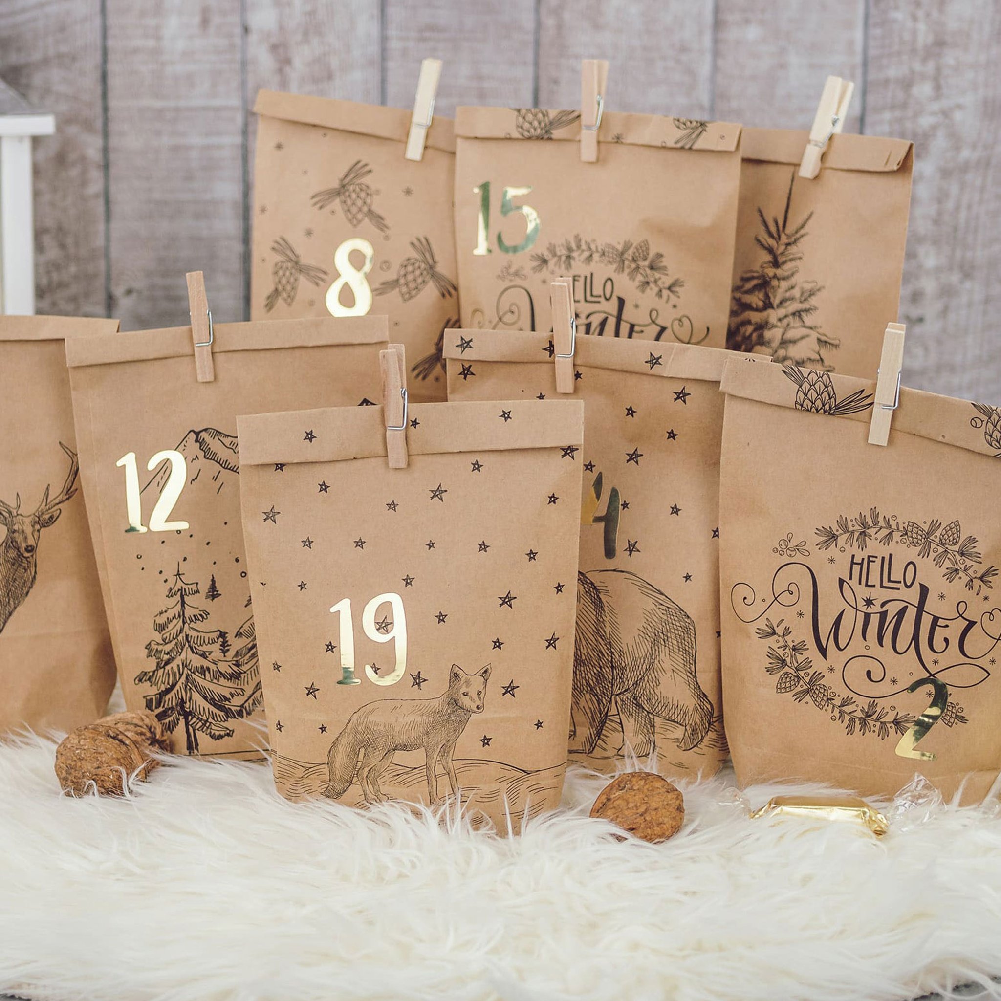 Tüten mit goldenen Zahlen 8, 15, 12, 19 und 21 und Hello-Winter-Aufdruck zwischen Walnüssen und Goldbonbons