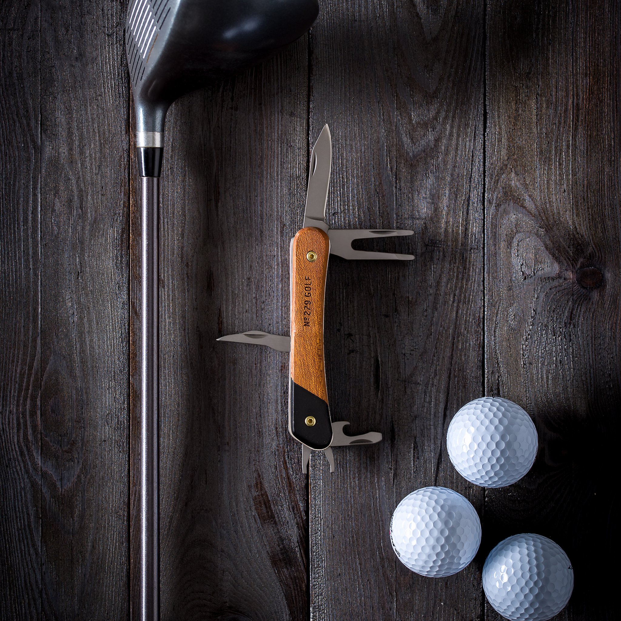 Outil de golf multifonction vu du dessus sur du bois sombre, près d'un club de golf et de trois balles blanches