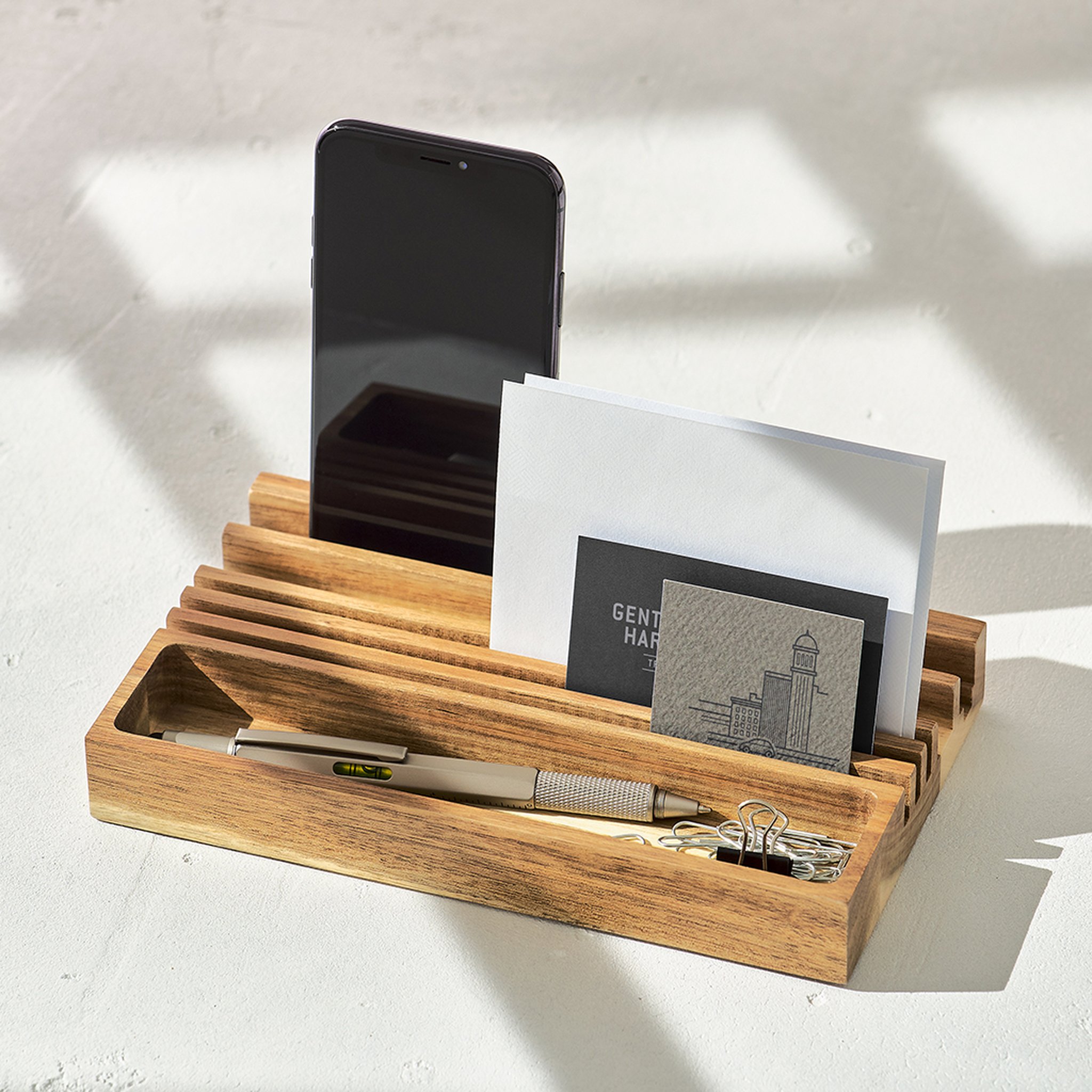 Organiseur en bois sur une table claire au soleil, avec téléphone, lettres, cartes de visite, stylo et trombones