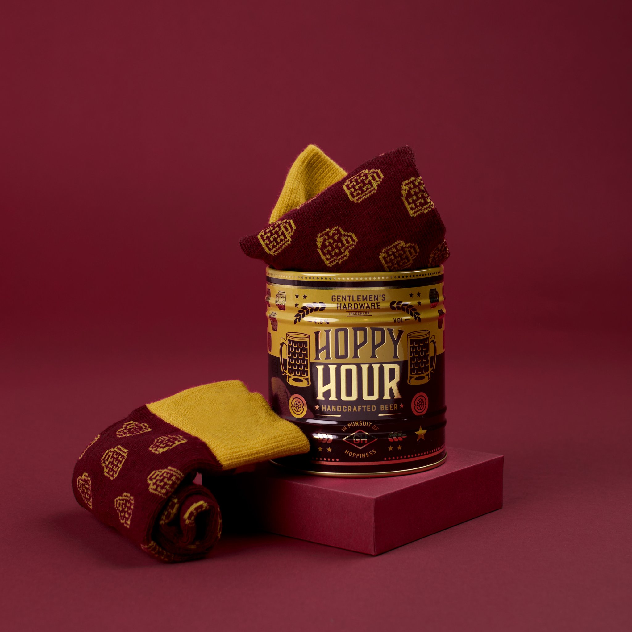 Socks in a Can - Beer styled on a burgundy backdrop, the tin on a plinth with one sock on top and one beside it